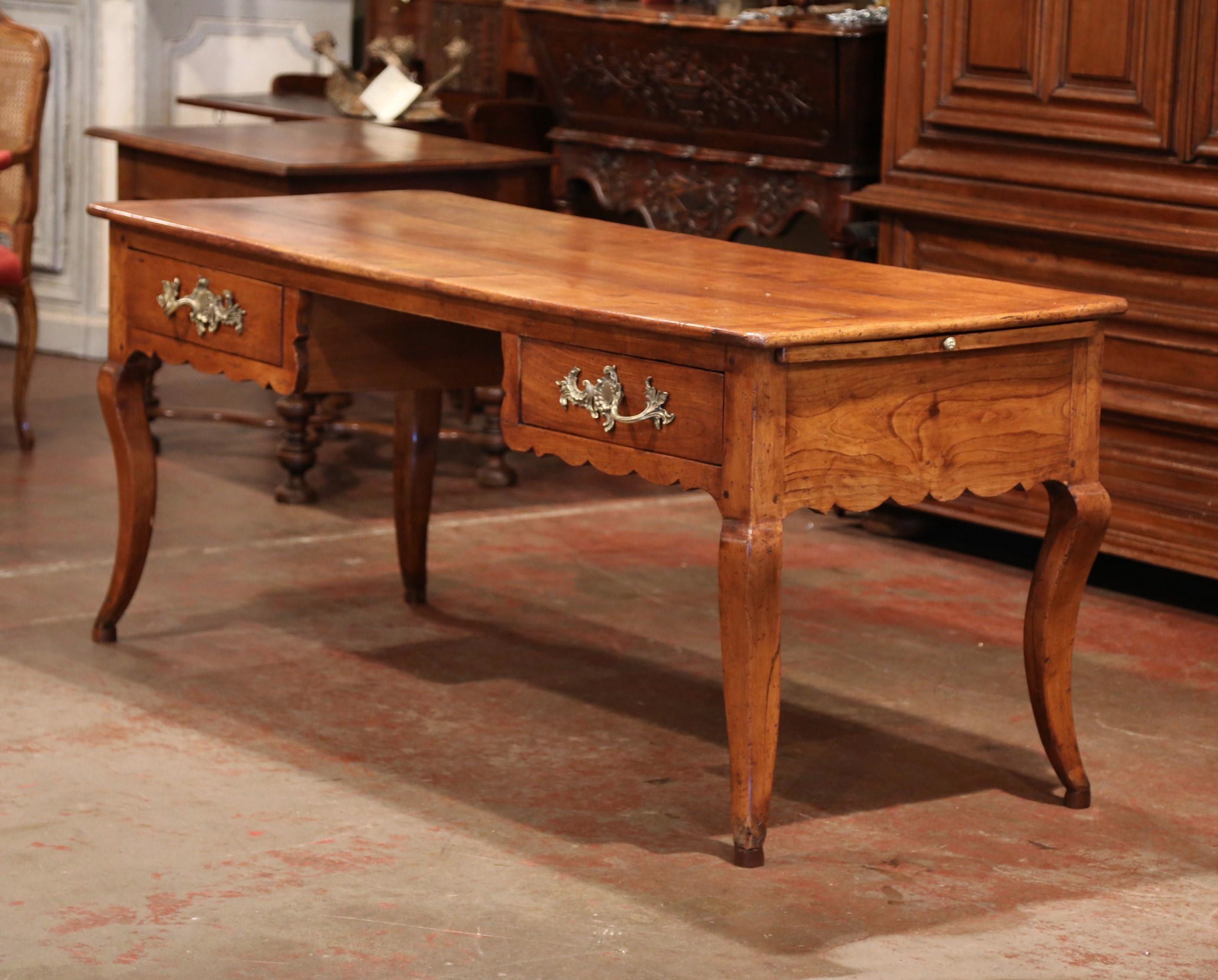 This elegant antique fruitwood desk was created in the Poitou region of France, circa 1790. Made of wild cherry timber, the large writing table sits on four cabriole legs over a decorative scalloped apron. The front has a wide opening with plenty of