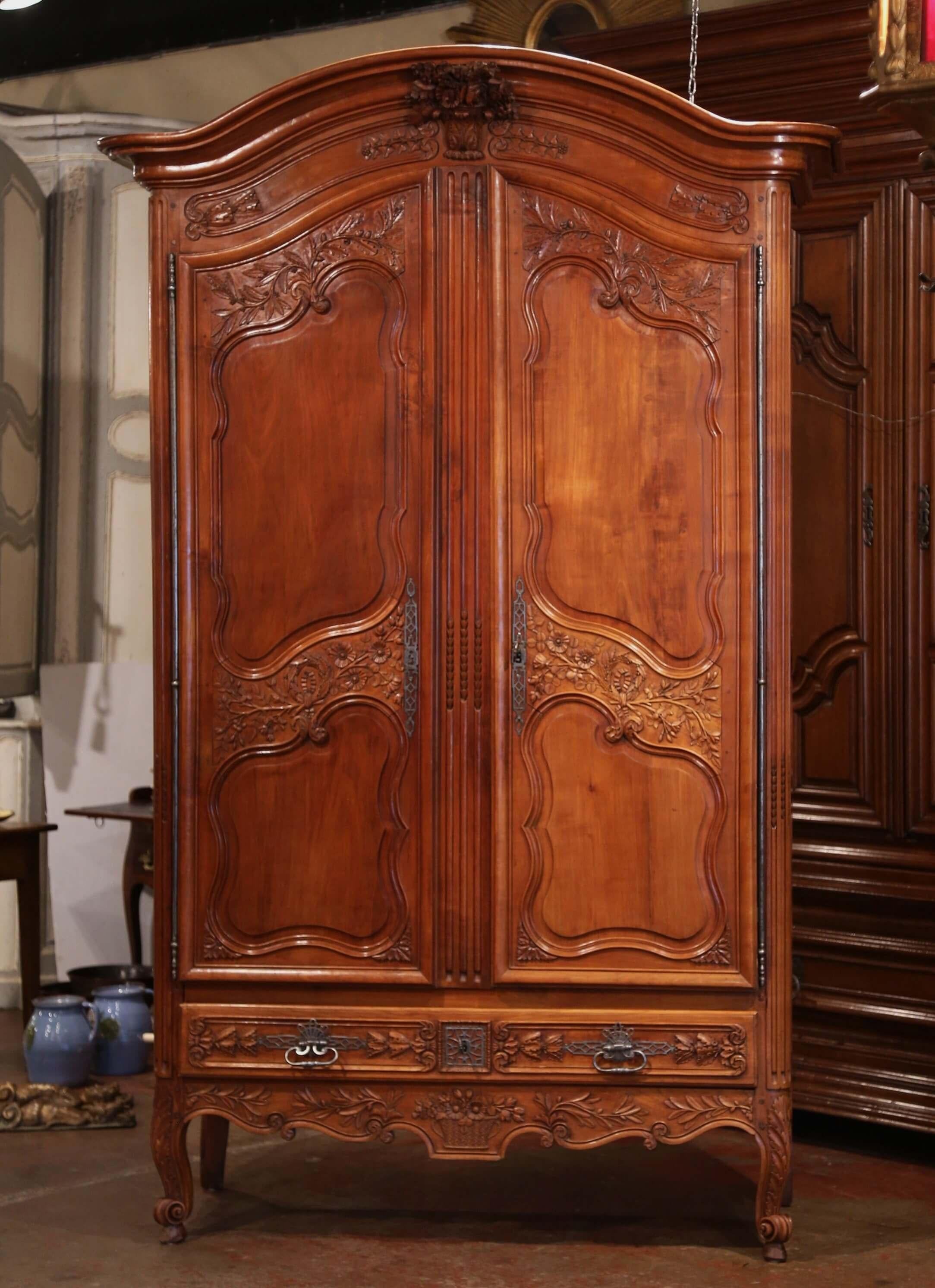 This important and elegant antique armoire was crafted in the Poitou region of France, circa 1770. The tall fruitwood cabinet stands on cabriole legs ending with escargot feet, and features a molded bonnet top over a fine carved center basket of