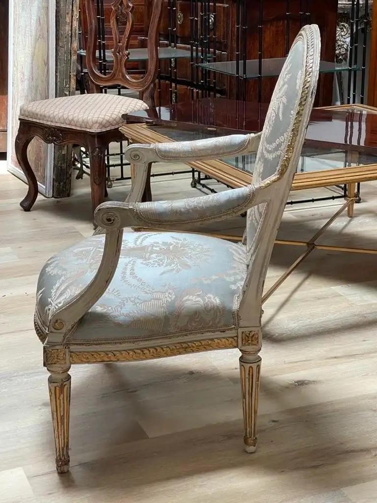 French Louis XV 18th Century Carved Gilt Wood Fauteuil Arm Chair, grey painted frame with gilt accents, oval medallion back with spiral carvings, open arms, shaped skirt, tapered and fluted legs. Grey, pink, and white urn and floral damask