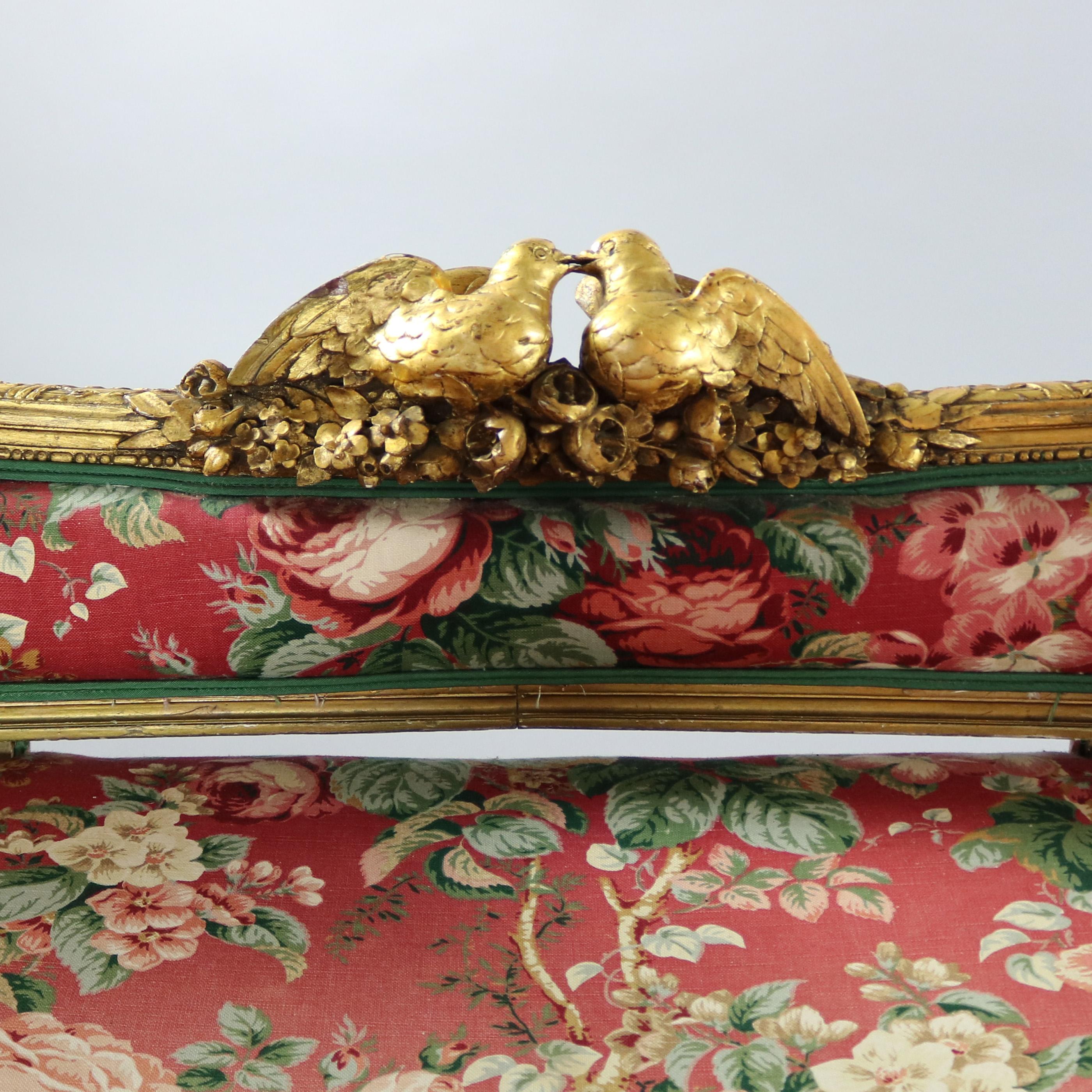 An antique 18th Century French Louis XV settee recamier features foliate giltwood frame with doves and foliate garland, floral interior upholstery and complimenting forest green exterior upholstery, floral and foliate garland skirting, raised on