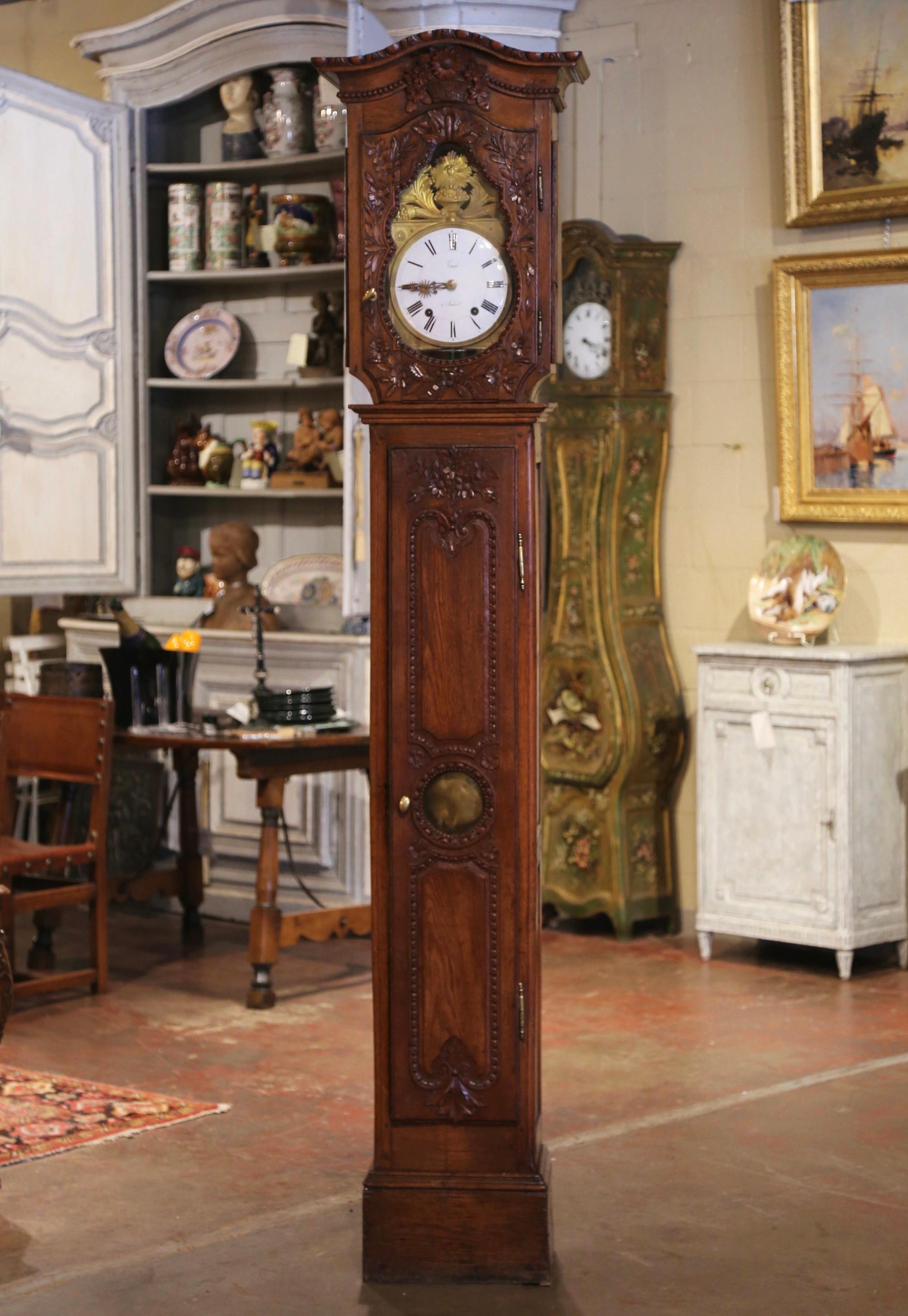 This elegant, antique long case clock was crafted in Normandy, France, circa 1780. The tall grandfather clock stands on a straight bottom plinth; it features a curved bonnet top over a carved flower basket and a highly carved glass door. The case