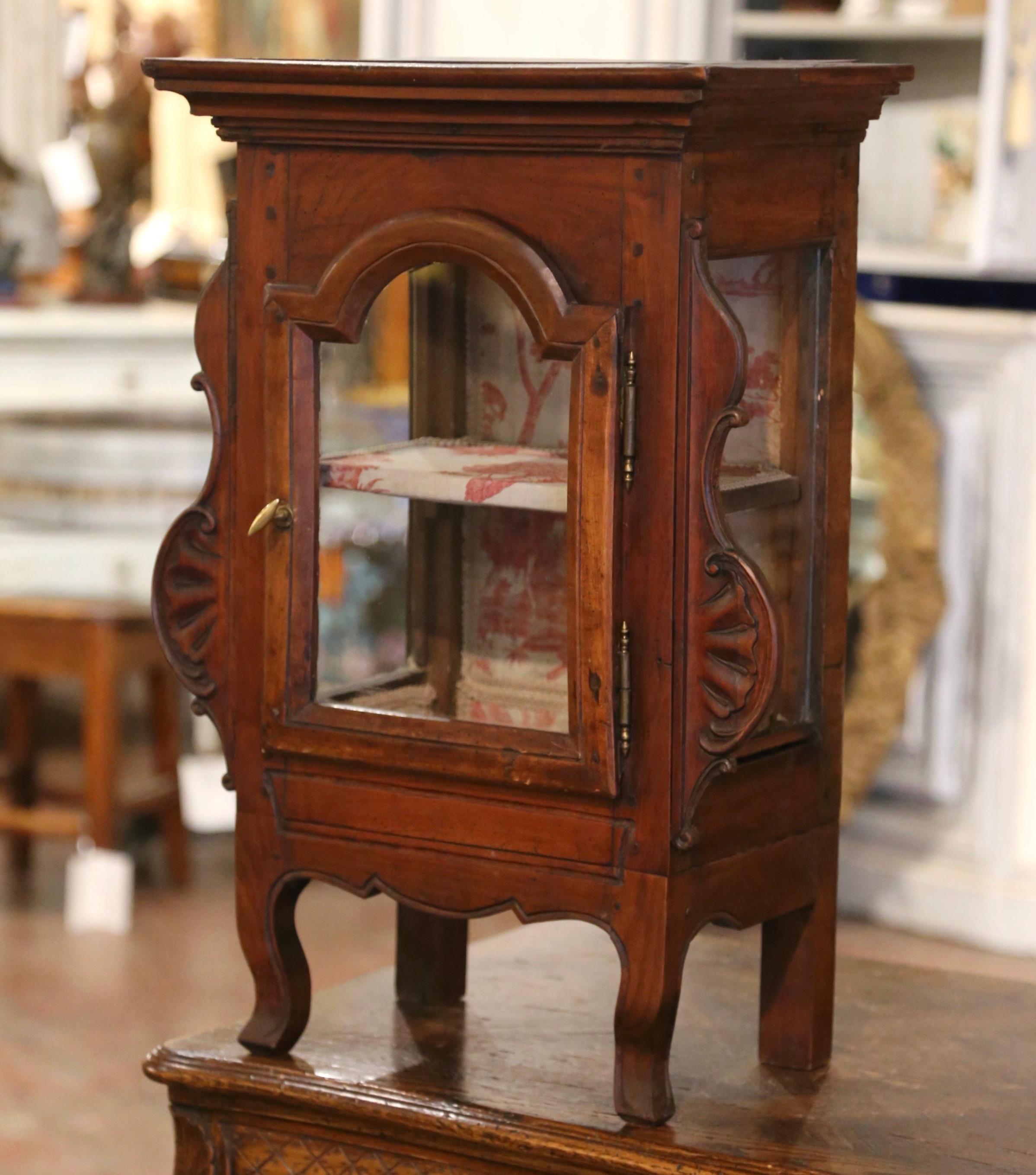 This elegant and petite antique vitrine was crafted in France, circa 1780. The hanging cabinet features front curved legs over a scalloped apron, and both sides are embellished with carved acanthus leaf motifs. The cabinet door with arched decor is
