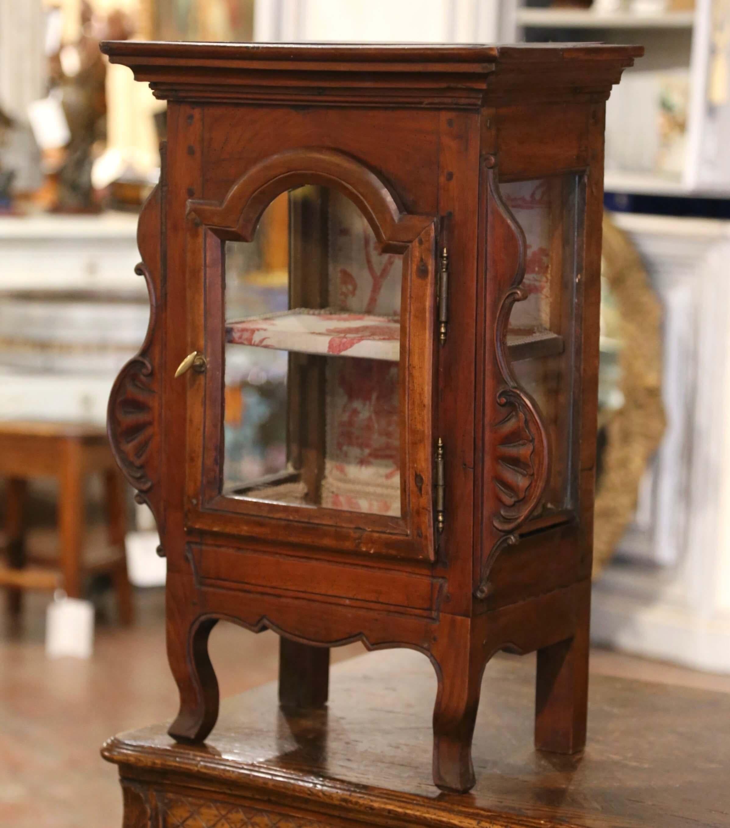 Esta elegante y pequeña vitrina antigua se fabricó en Francia hacia 1780. El armario colgante presenta patas curvadas delanteras sobre un delantal festoneado, y ambos lados están adornados con motivos tallados de hojas de acanto. La puerta del