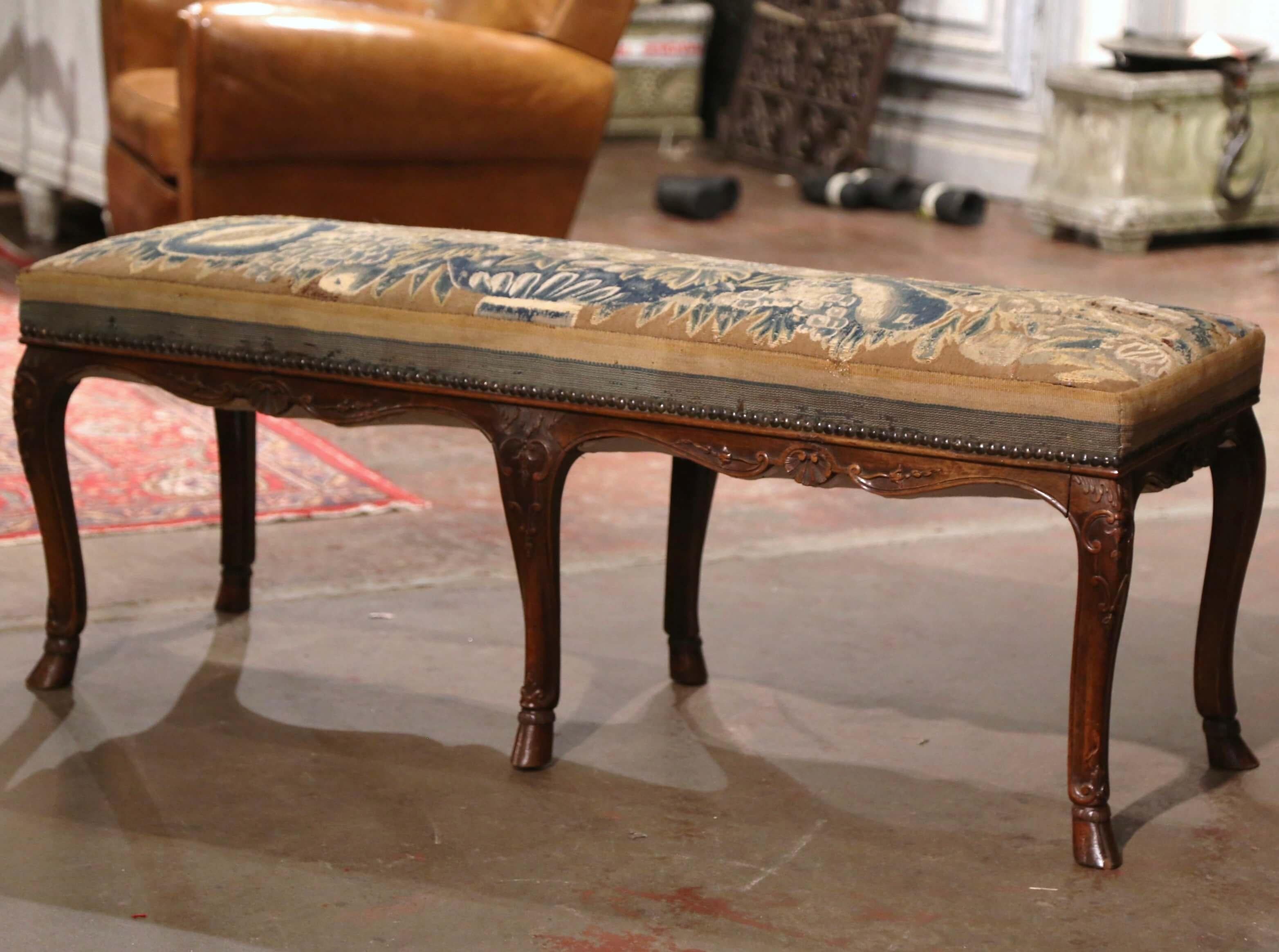 Place this elegant antique bench at the foot of your bed, or use it for extra seating. Crafted in Provence, France circa 1780, and built of walnut, the fruit wood bench stands on six cabriole legs ending with hoof feet, and decorated with delicate