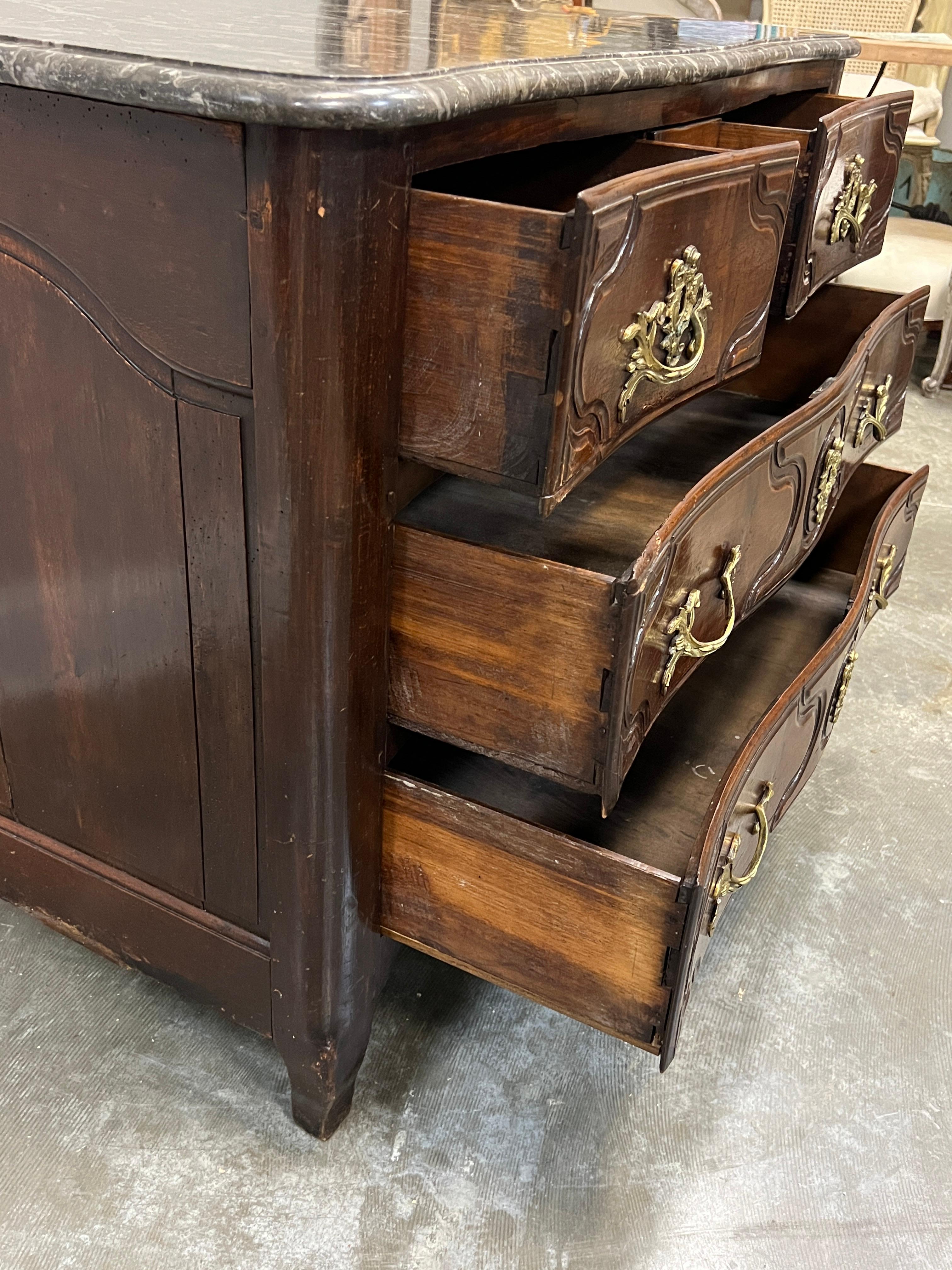 Classic Louis XV French commode of provincial style with two top drawers over two bottom drawers. The drawers are decorated with carved, lozenge shaped decoration and have hardware which appear original. The marble top is original and is black with