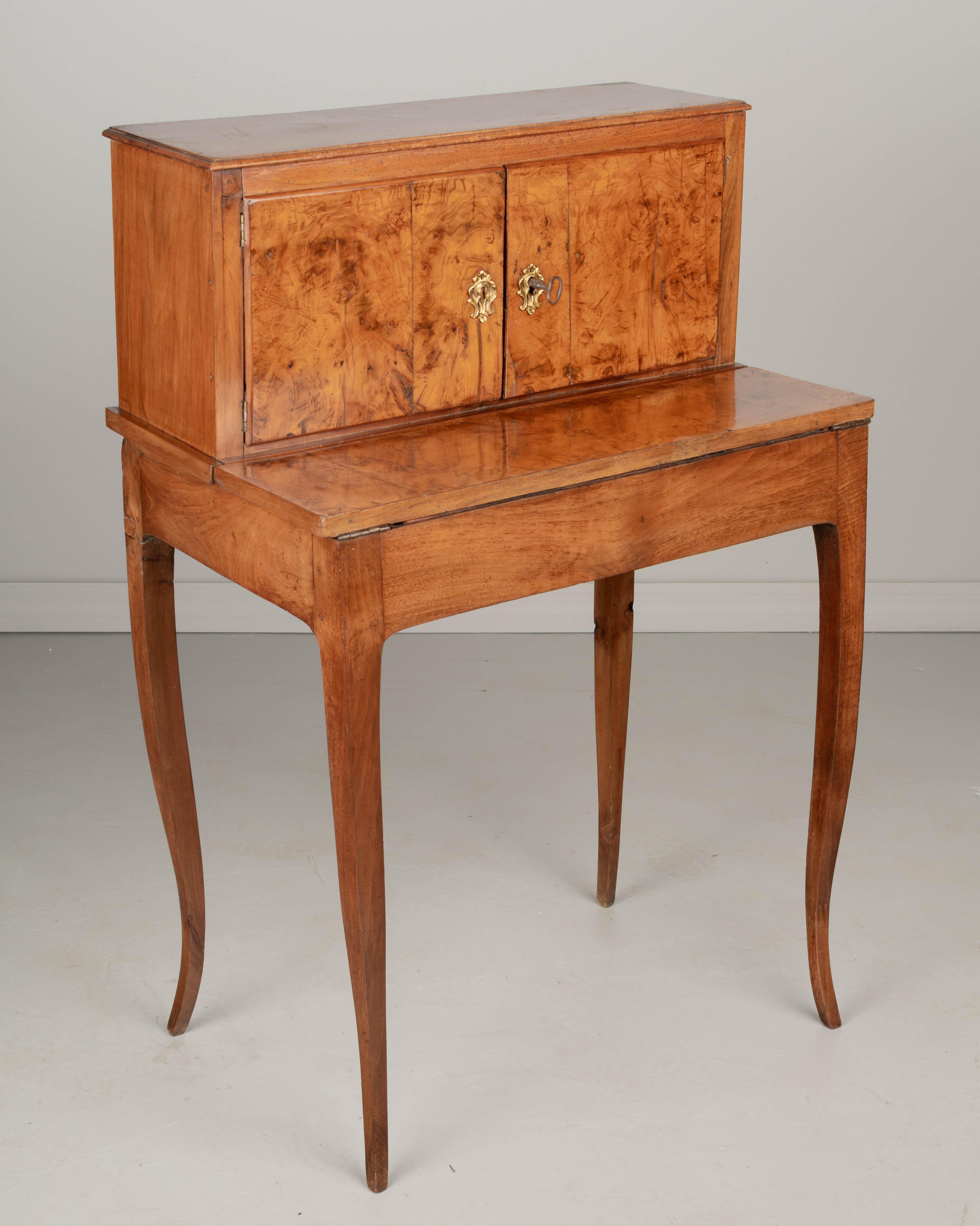 A late 18th century French Louis XV style small lady's desk with hinged drop down leather top writing surface. Made of walnut and in two parts with small top cabinet with one interior shelf. Cabinet doors and table surface have beautifully patterned