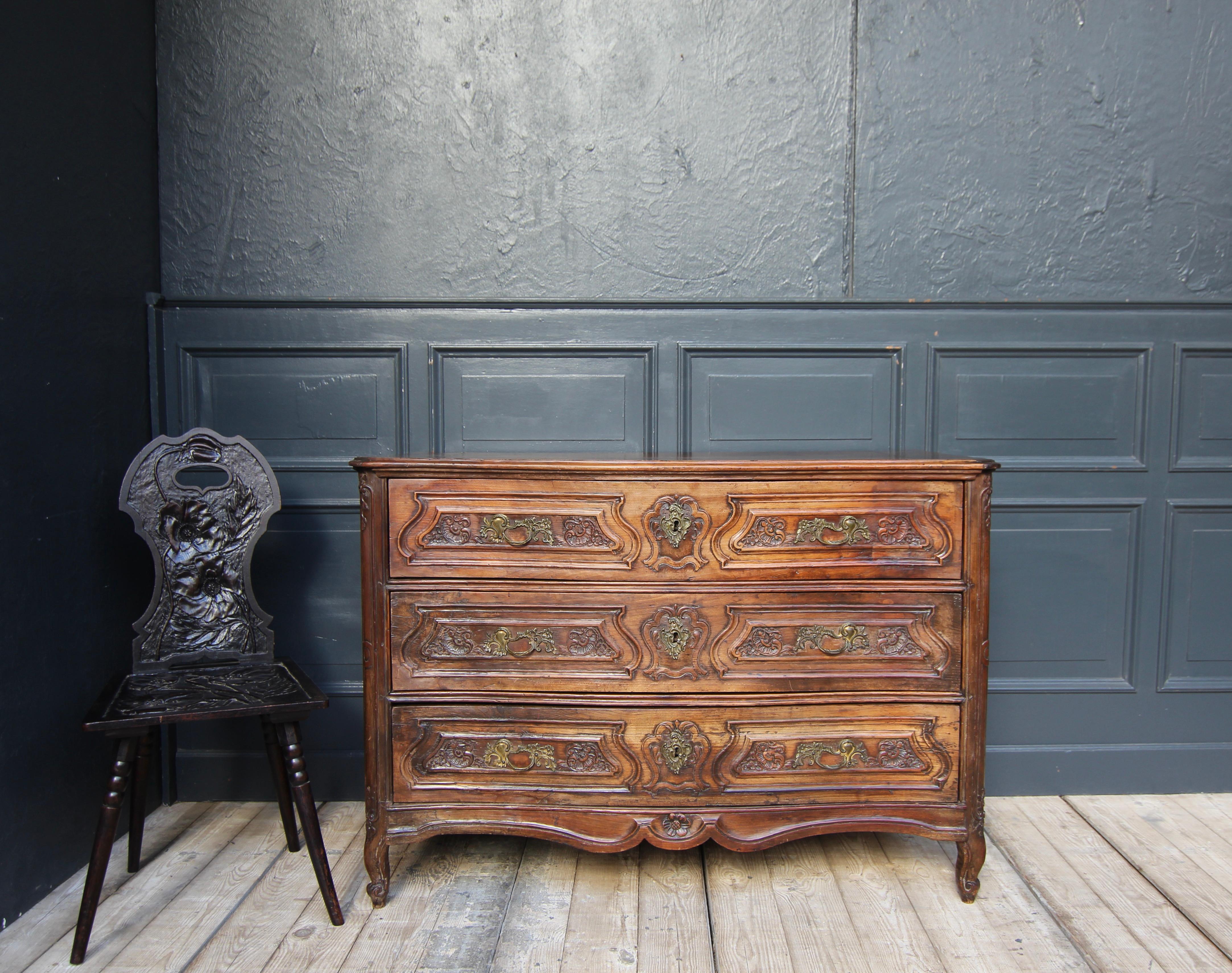A 18th century French Louis XV chest of drawers. Solidly made of cherry wood and hand carved with floral and ornamental motifs. Restored condition.

Slightly trapezoidal lateral coffered corpus with 3 drawers and profiled top. Nobly S-shaped