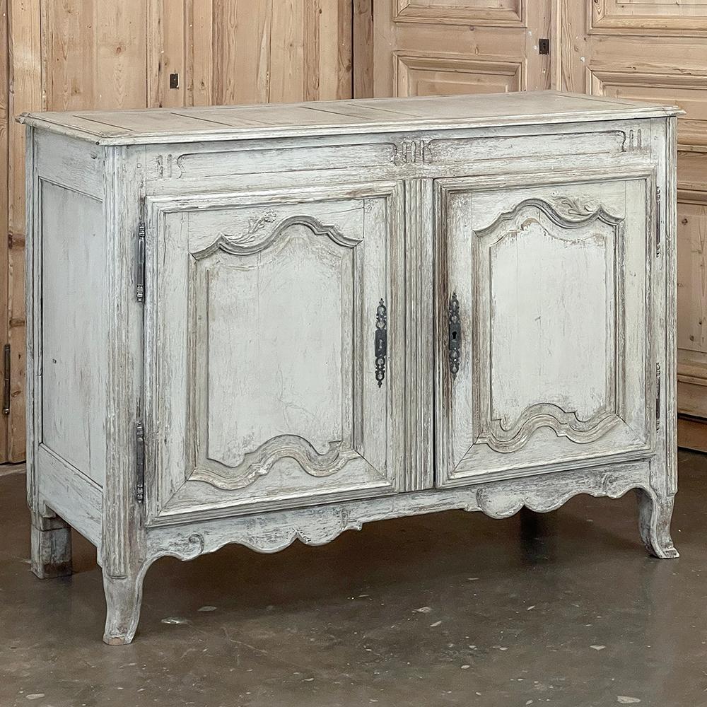18th Century French Louis XV Painted Buffet features a very tailored version of the style, with timeless French scrollwork in the door panels, apron and legs, and just a hint of foliate carvings.  The patinaed and somewhat distressed painted finish