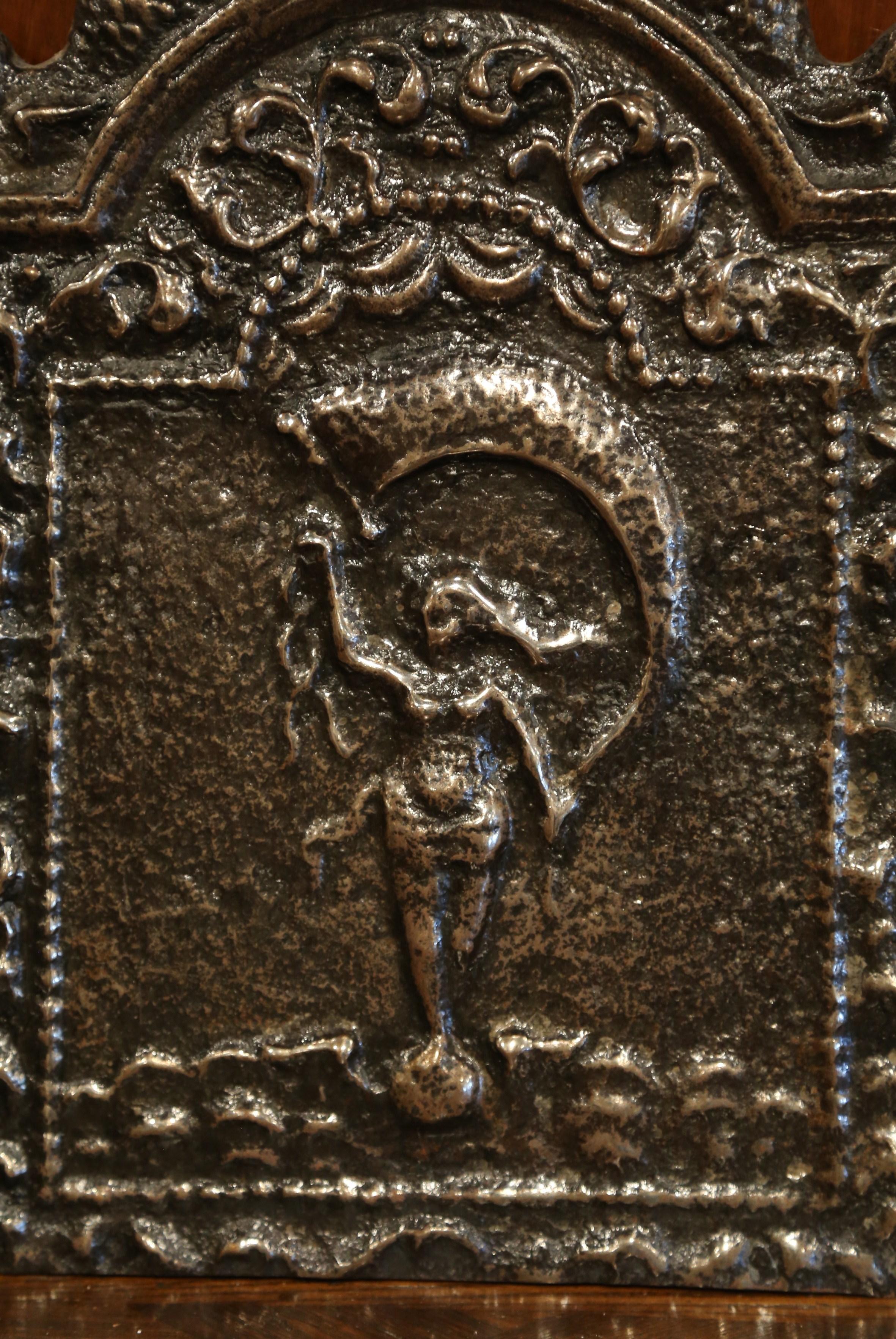 Decorate a fireplace with this antique fireback. Crafted in France, circa 1780, the mythological iron plaque has an arched top flanked with dolphin figures on both sides. The central composition features a crowned goddess waving a large flag