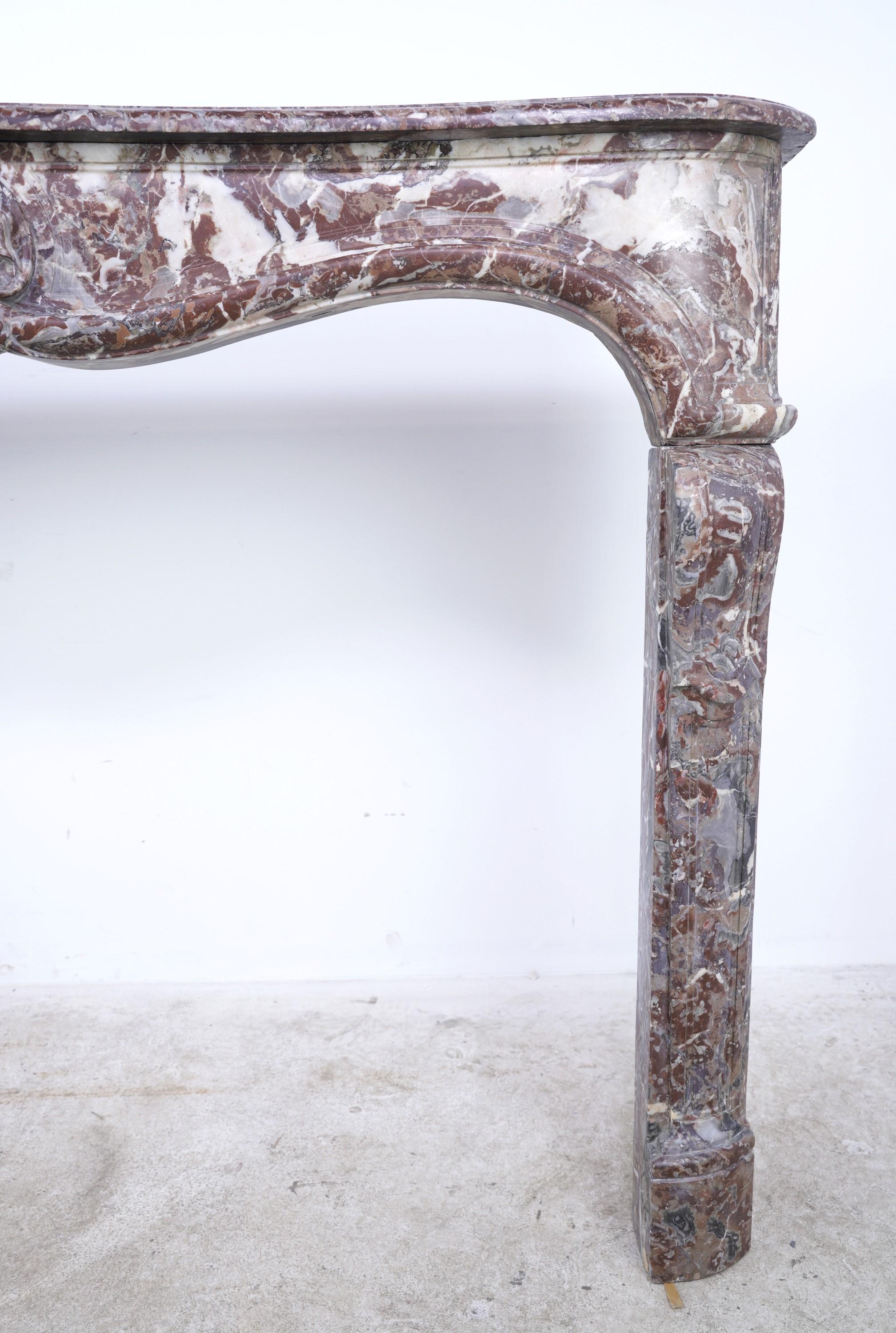 Original 18th Century Louis XV hand carved rouge royal marble mantel featuring white and grey veining. The serpentine front apron has a unique heavily carved center design and a sharply curved lower molding continuing across both side pieces. Each
