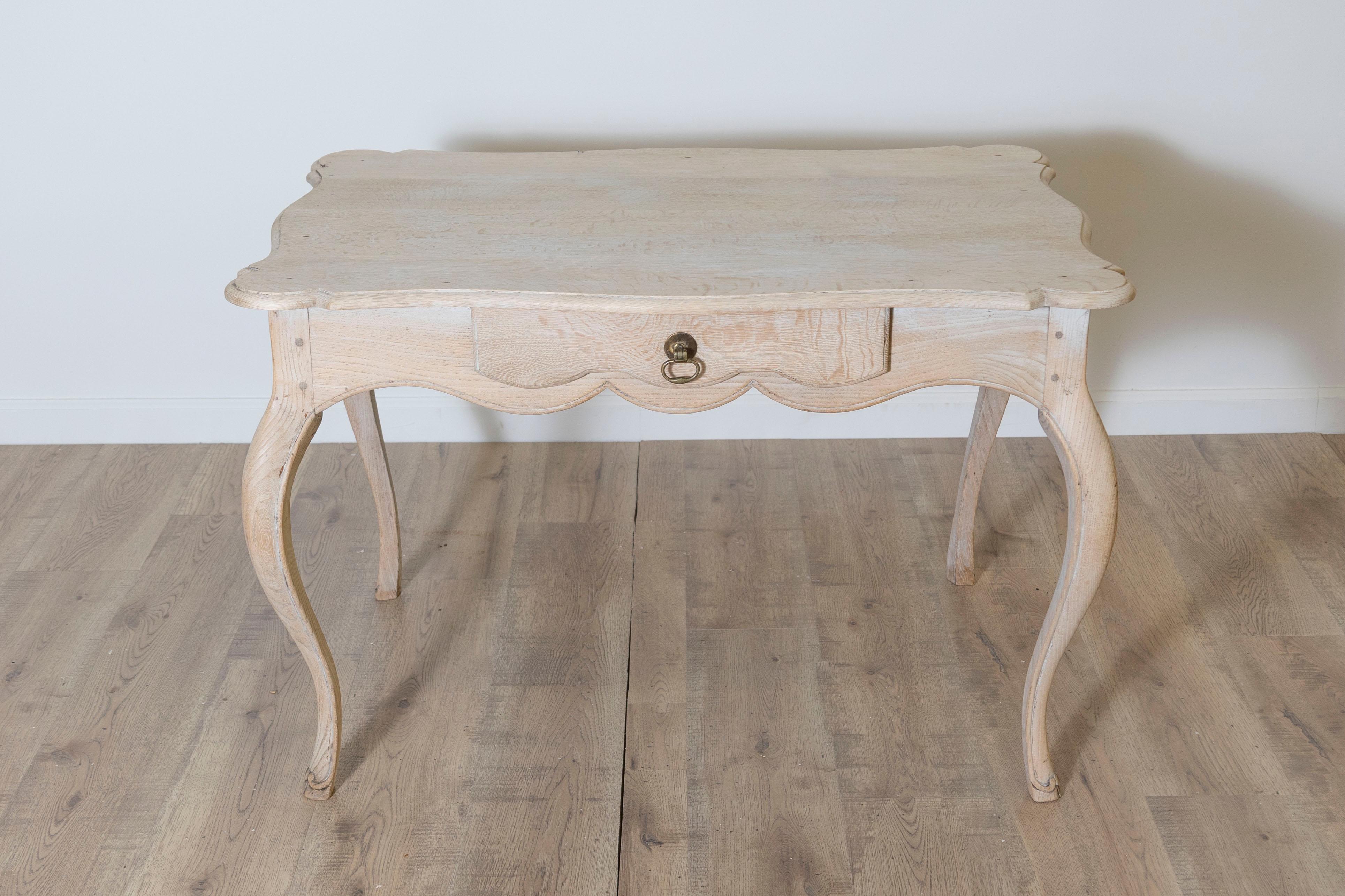 Cette charmante table d'appoint Louis XV française du XVIIIe siècle met magnifiquement en valeur l'élégance et la fluidité de la période rococo. Fabriquée en chêne massif, la table présente un tablier festonné avec un seul tiroir, orné d'une tirette