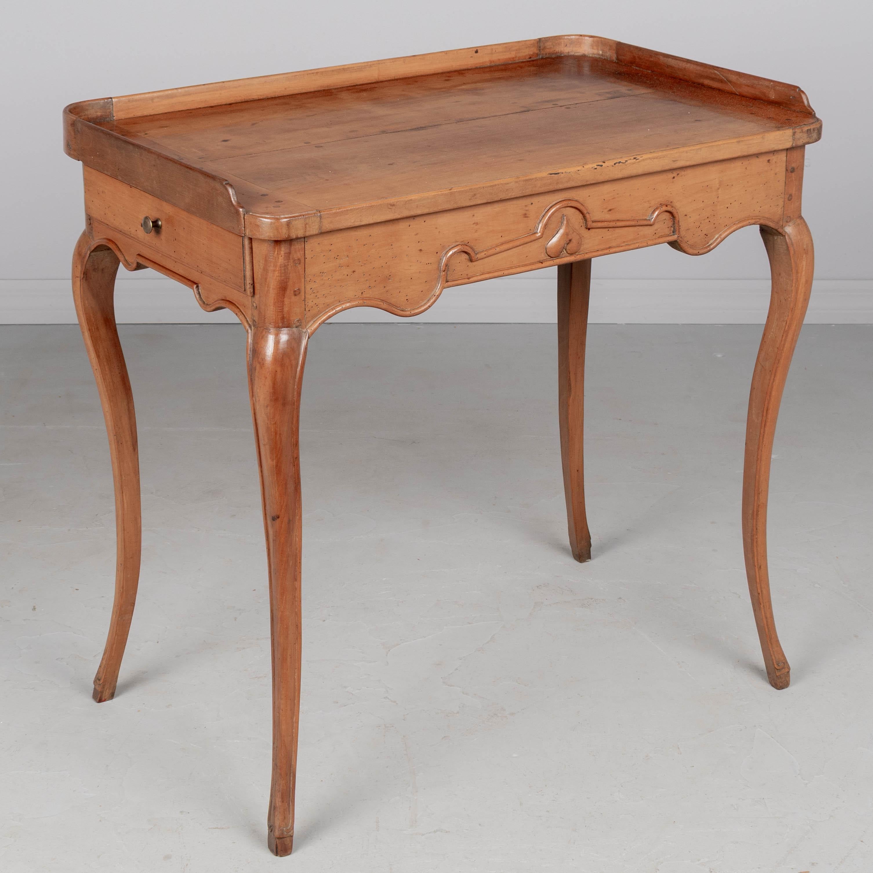 Table d'appoint ou petit bureau Louis XV du XVIIIe siècle en poirier massif avec galerie surélevée sur trois côtés et pieds robustes et minces en cabriole incurvée. Tablier festonné sculpté à la main et décoré d'un cœur. Deux tiroirs à queue