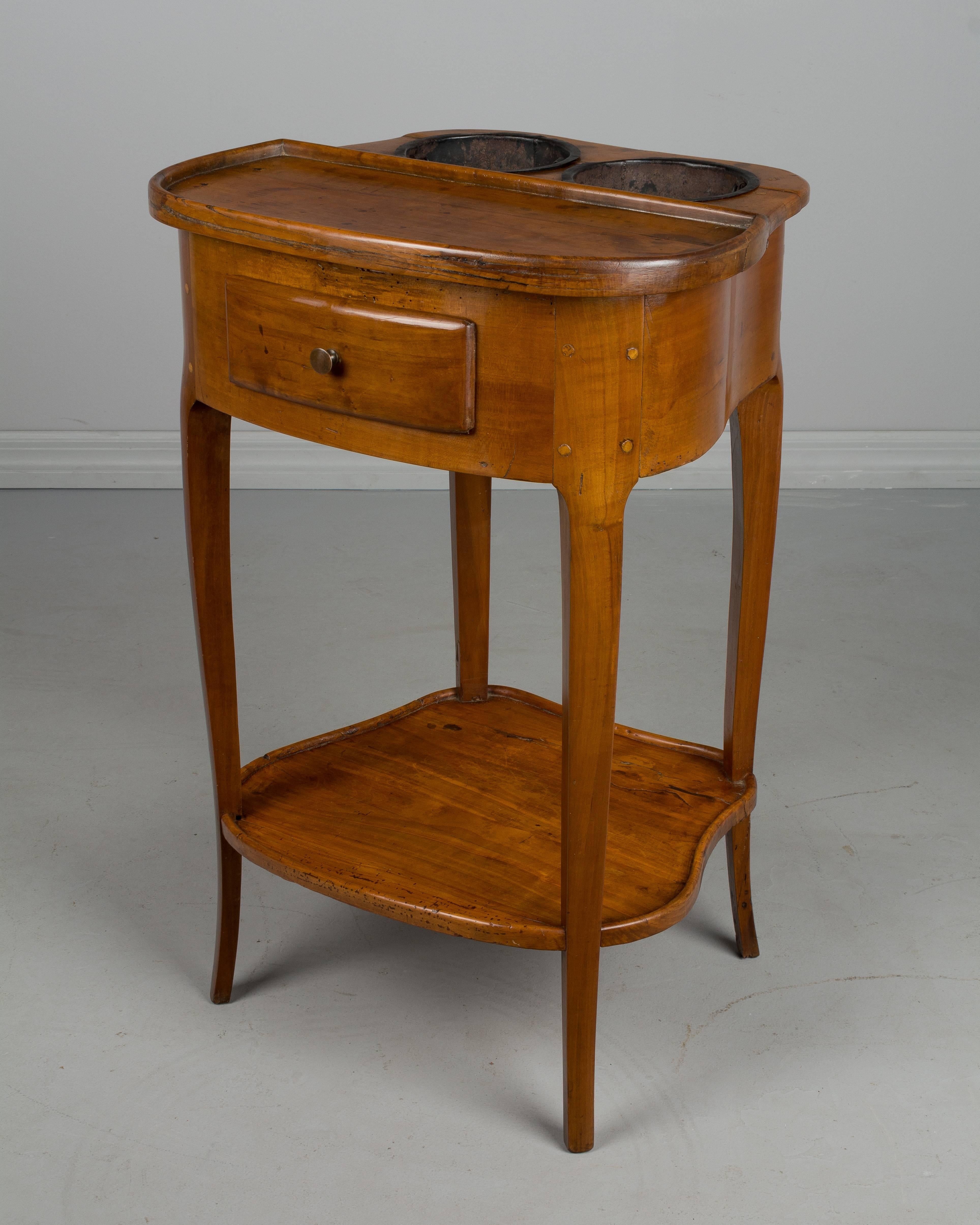 An 18th century French Louis XV style Rafraîchissoir side table with elegant curved shape and cabriole legs, a single dovetailed drawer and lower shelf. Made of solid cherrywood with pegged construction and warm waxed patina. Original removable tin
