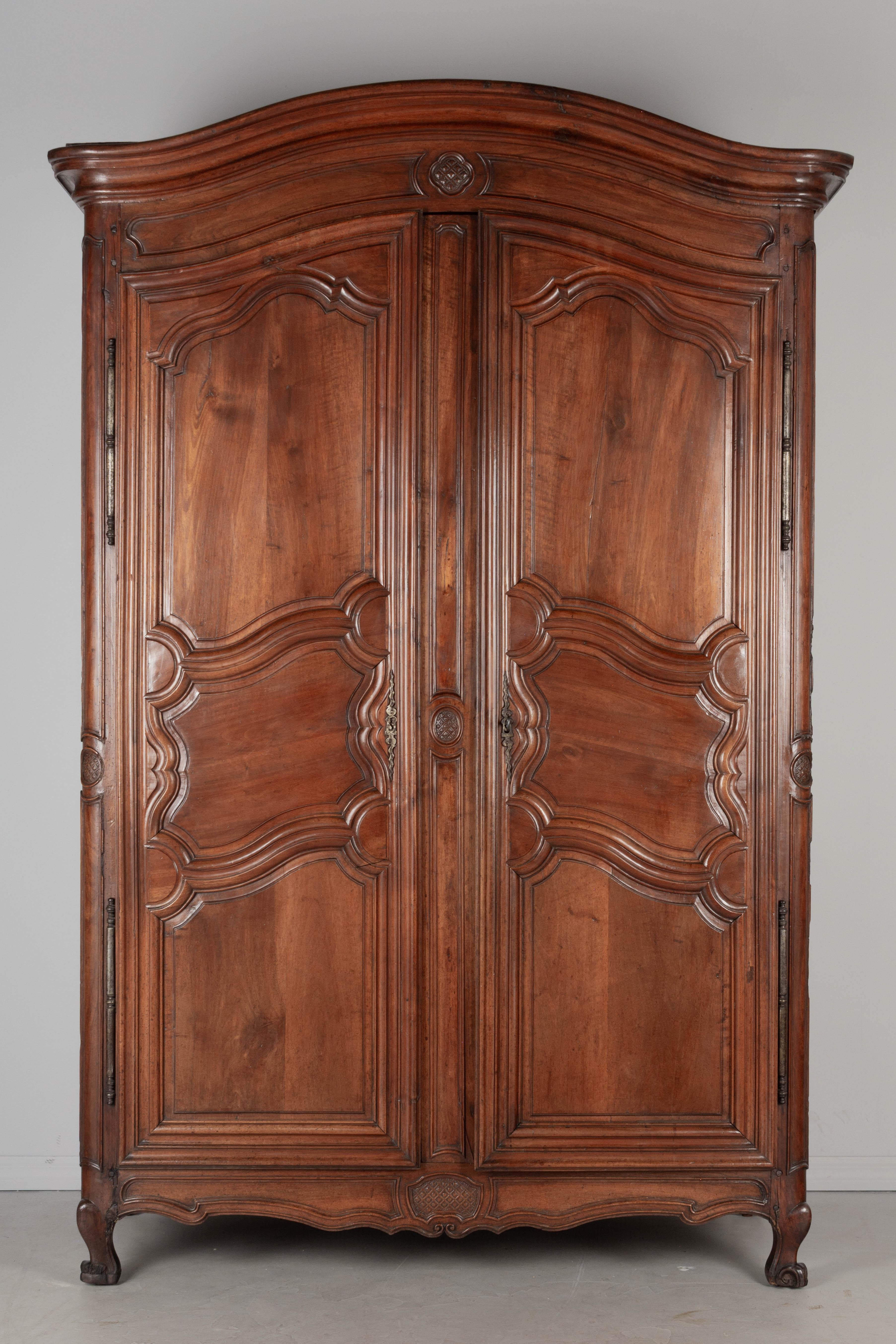 A large 18th Century French Louis XV armoire from Burgundy with chapeau de gendarme crown. Made from thick planks of solid walnut with twelve raised panels. Simple hand-carved decorative details on the apron and crown and on the rounded front