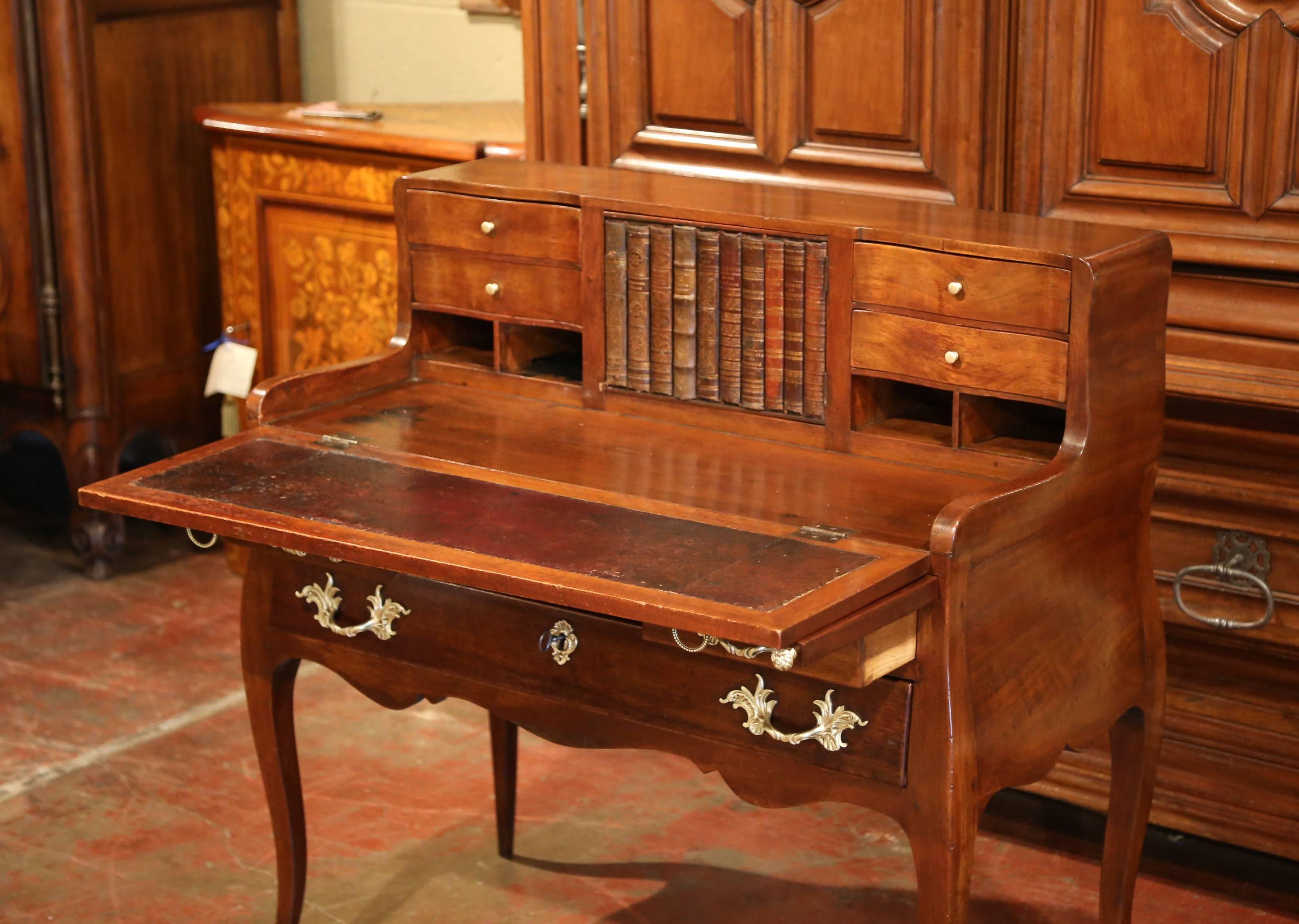 This elegant antique fruitwood commode-secretary was crafted in Paris, France circa 1780; the ladies desk with bombe sides, features nine drawers with a faux book center door. The top folds down to reveal a black leather writing surface. The top