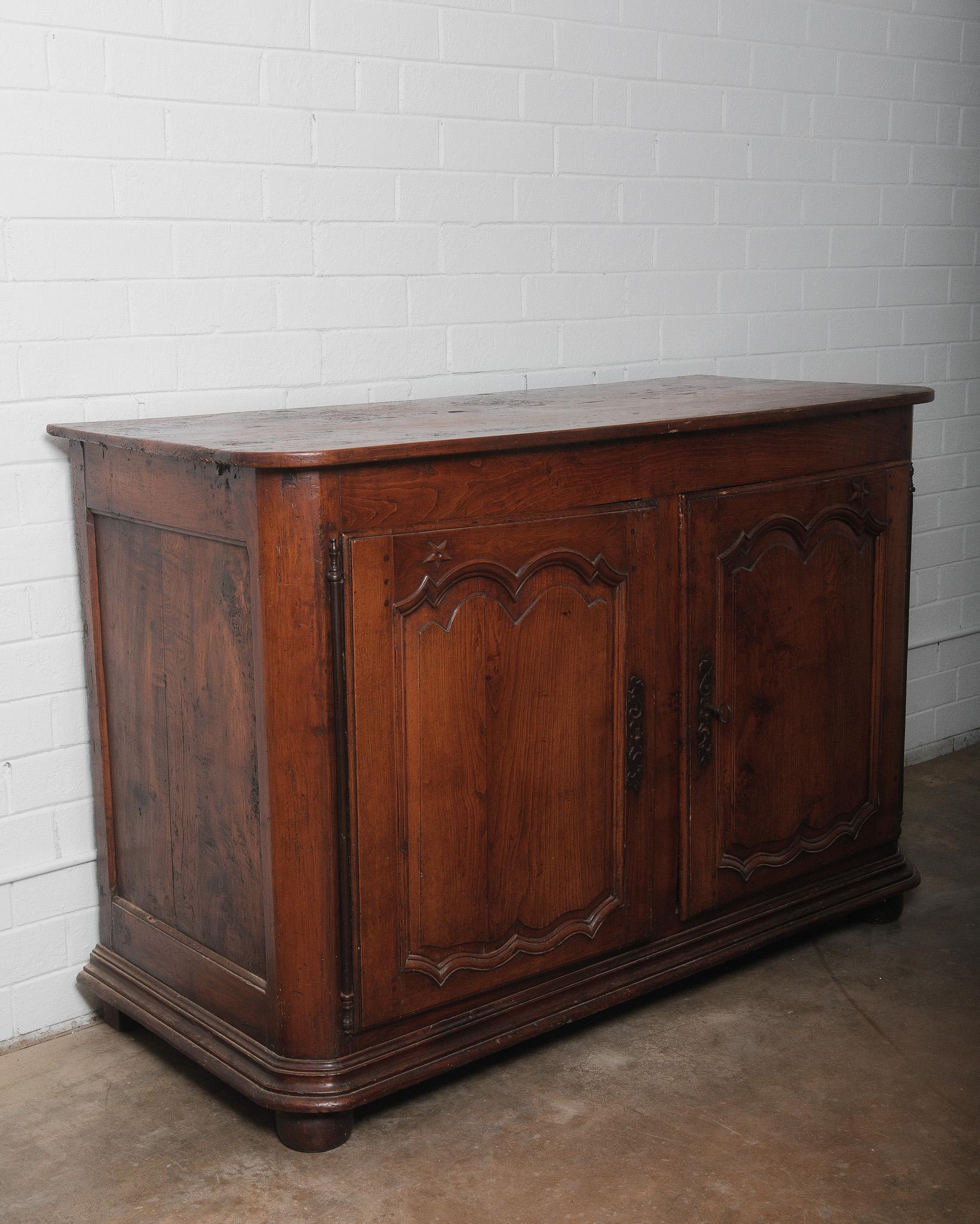 This exquisite 18th-century French Louis XV walnut buffet is a remarkable example of period craftsmanship and elegance. Featuring two paneled doors with scalloped moldings and hand-carved star motifs, this piece exudes timeless charm. The original