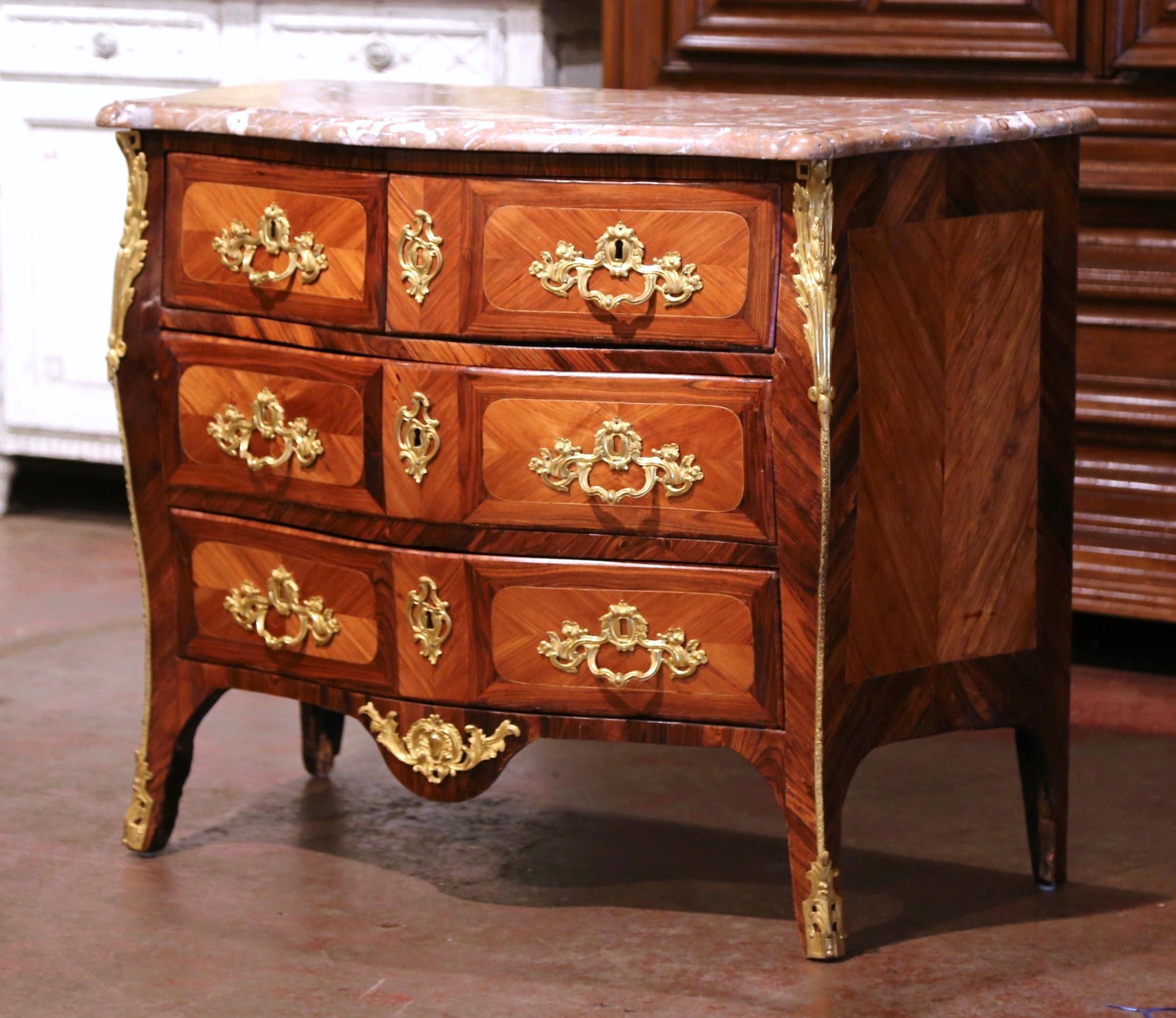 Crafted in Burgundy France circa 1780, the antique fruitwood commode stands on curved feet ending with bronze mounts over a scalloped apron decorated with a bronze shell and leaf motif mount. The chest features three rows across the front with four