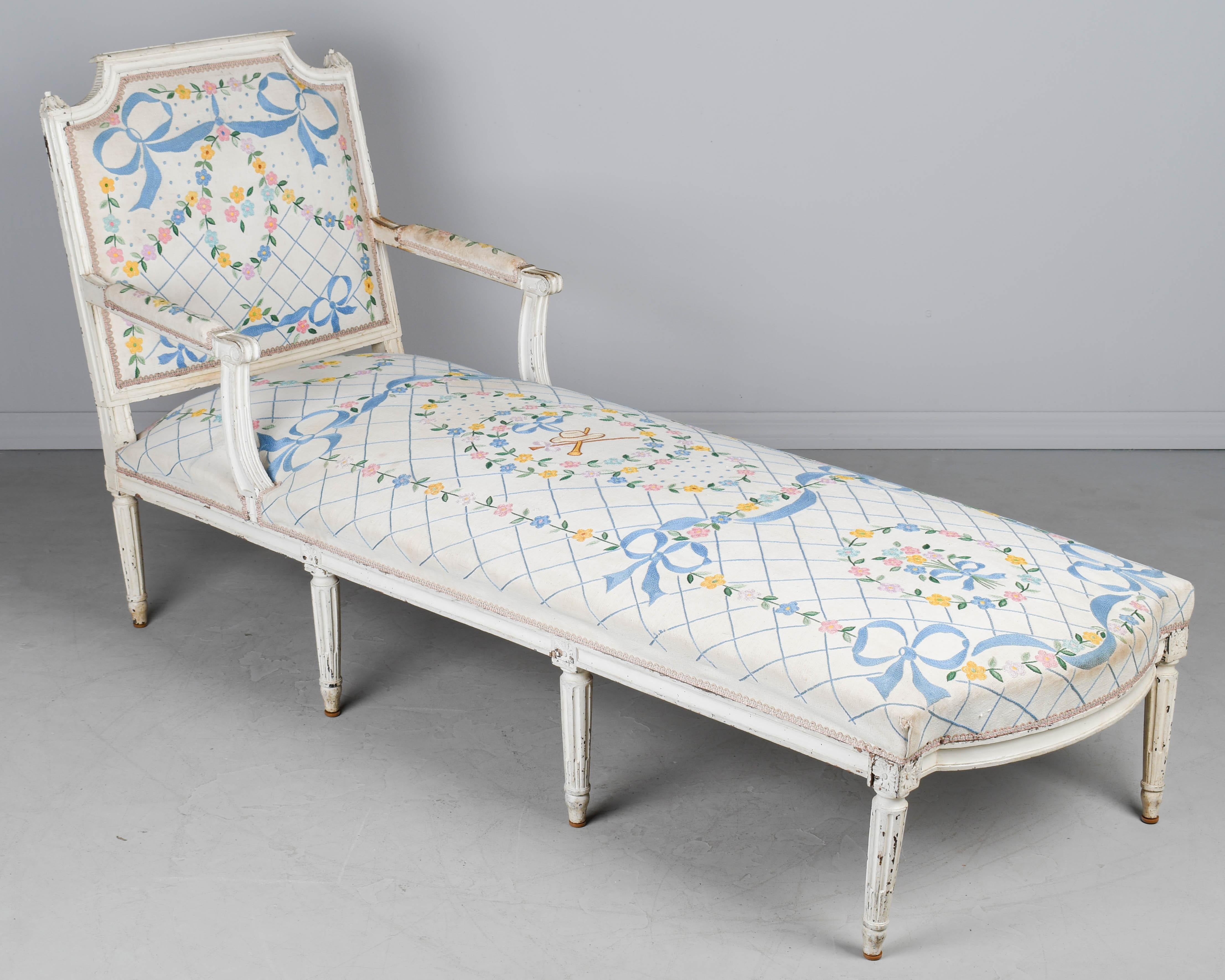 A late 18th Century French Louis XVI style chaise longue, along with two small stools each covered in old white linen fabric with hand-made tambour embroidered pink and yellow flower garlands and blue ribbons and bows. Upholstery is old and slightly