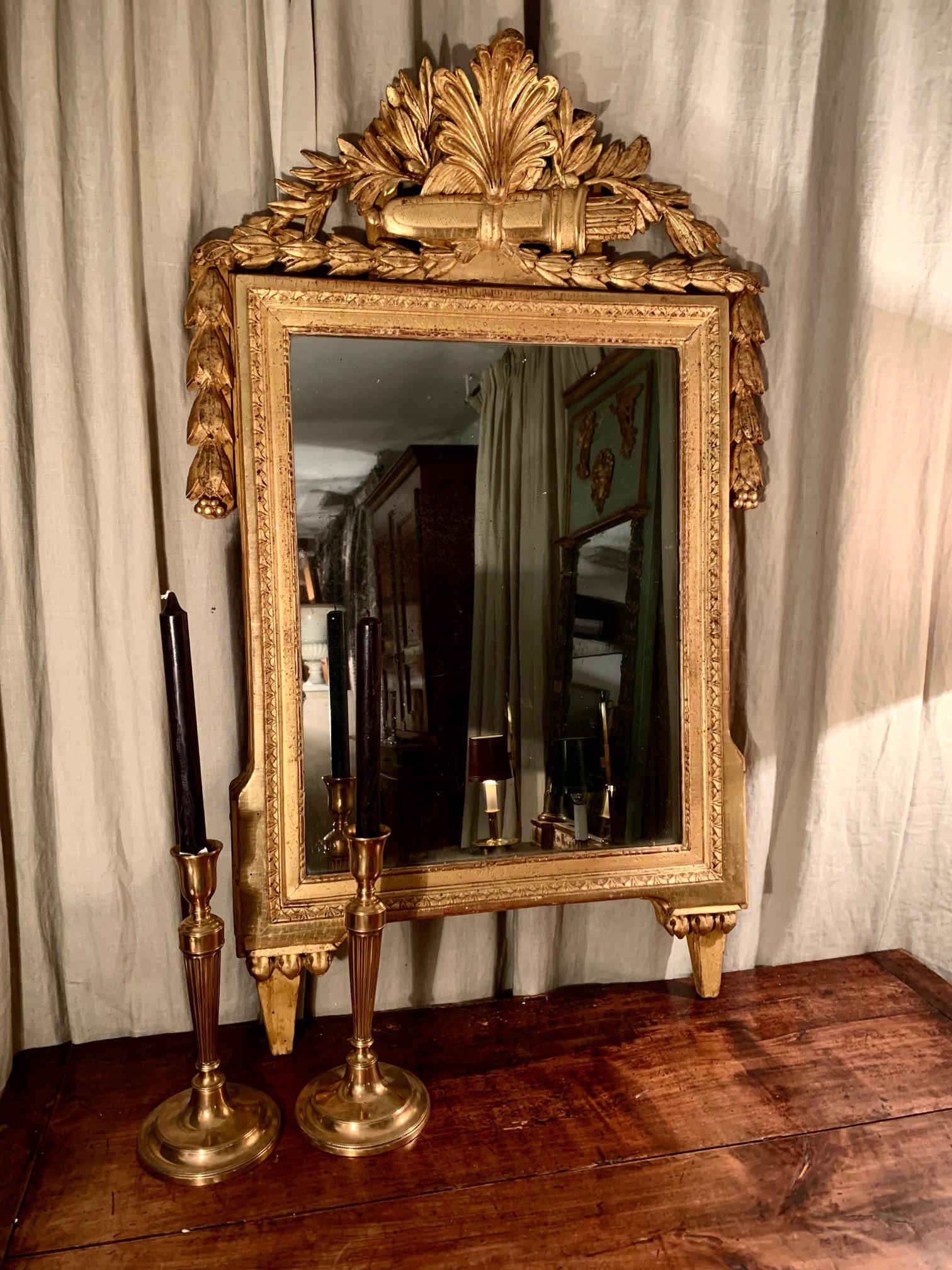 Mirror from France, hand-carved in gilt wood, from the LouisXVI Directory era or period, in the upper part carved in the shape of a vegetable shell and just below a carving of arrows in its case, which possibly symbolizes the arts., on its sides and