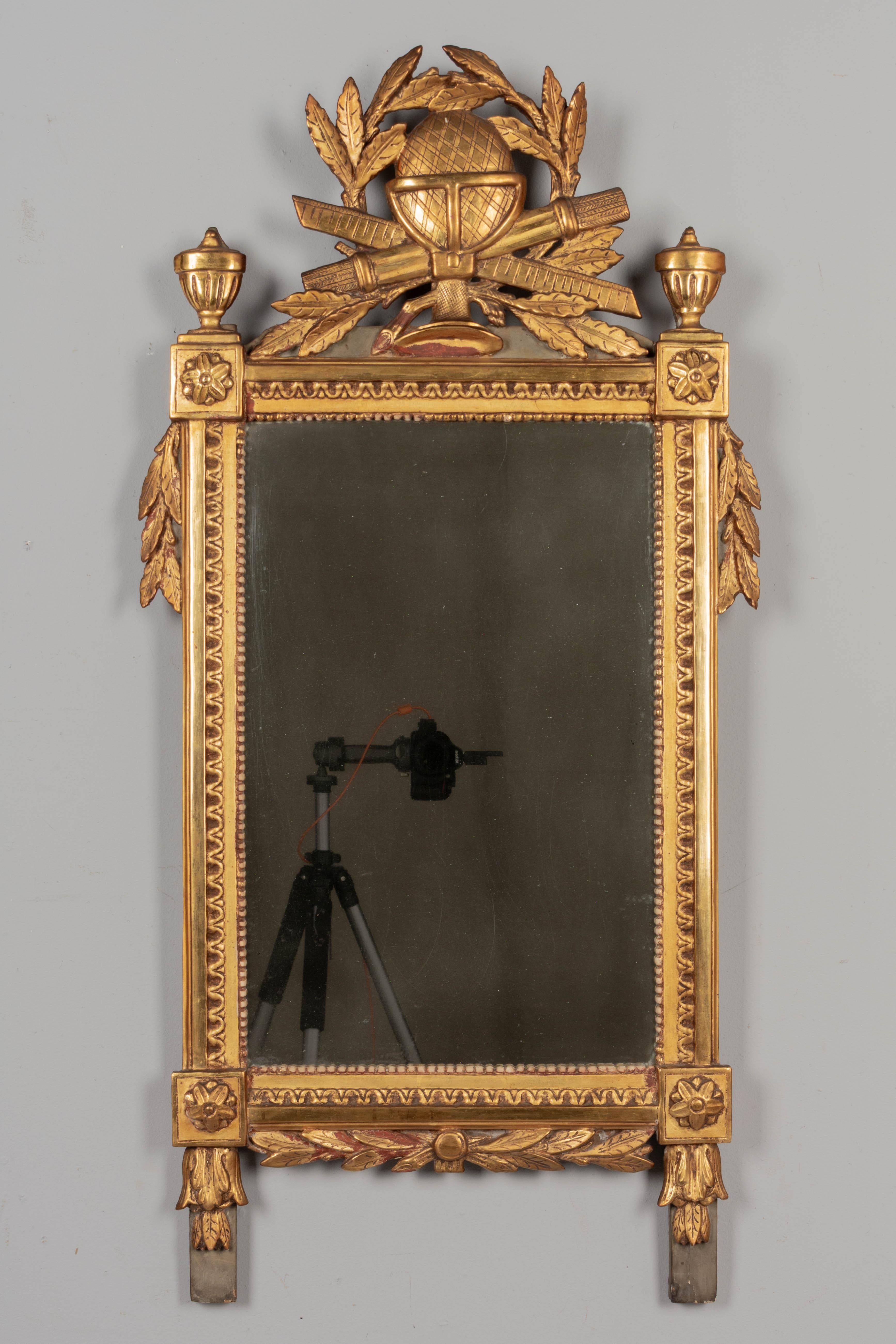 An 18th century Louis XVI French giltwood mirror. Carved pine frame with warm gilt finish and verdigris painted details. Beautifully detailed hand-carved crest with an orb surrounded by a laurel wreath and garlands that drape down the sides, corner