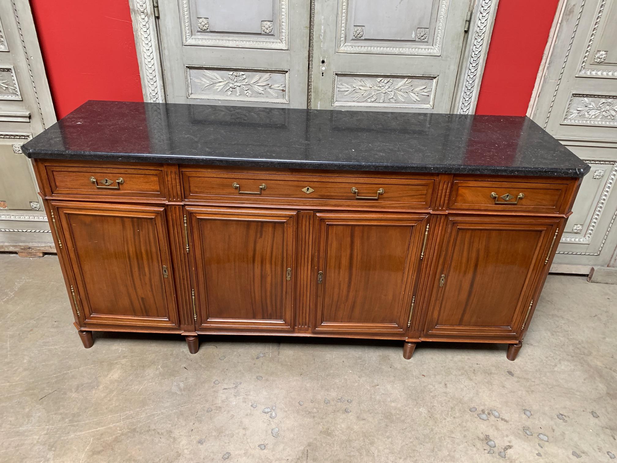 A large 18th century Parisian mahogany buffet with a newer black stone top. This French Louis XVI buffet is comprised of four doors and four drawers that are adorned with bronze hardware. This large scaled piece has ample storage and surface space.
