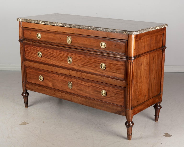 An 18th century Louis XVI French commode, or chest of drawers, made of solid walnut. Three dovetailed drawers with original brass hardware, no keys. The face of the two bottom drawers is solid Cuban mahogany with beautiful satin grain. The interior
