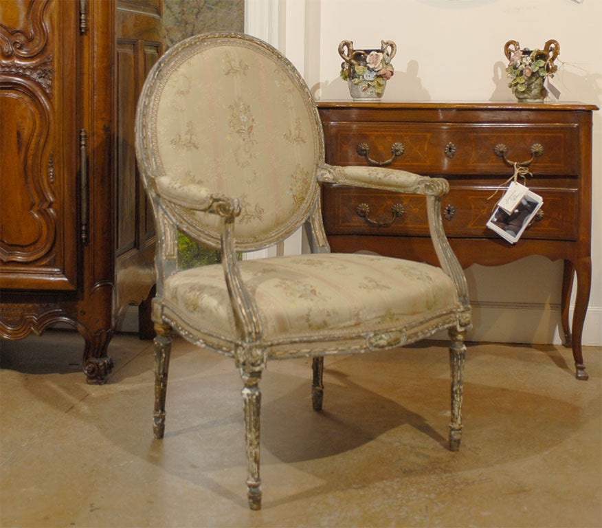 A French Louis XVI period painted and carved wooden fauteuil from the late 18th century, with oval back, floral fabric and distressed finish. Born in France during the reign of King louis XVI, this armchair features an oval back, adorned with