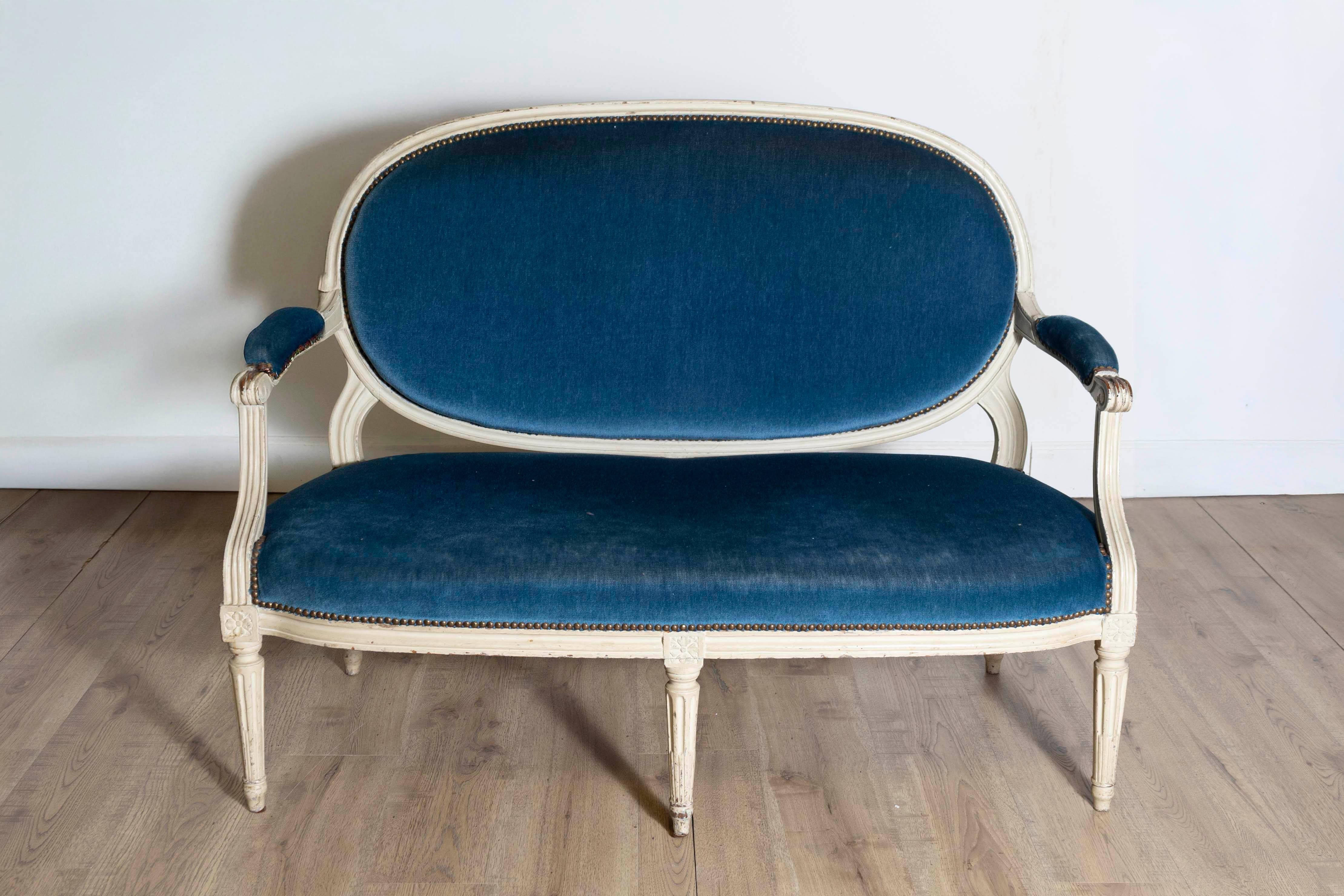 This elegant 18th century French Louis XVI period canapé, circa 1790, exemplifies the neoclassical style of the era. The refined oval backrest and delicately carved frame are painted in a soft antique white, creating a striking contrast with the