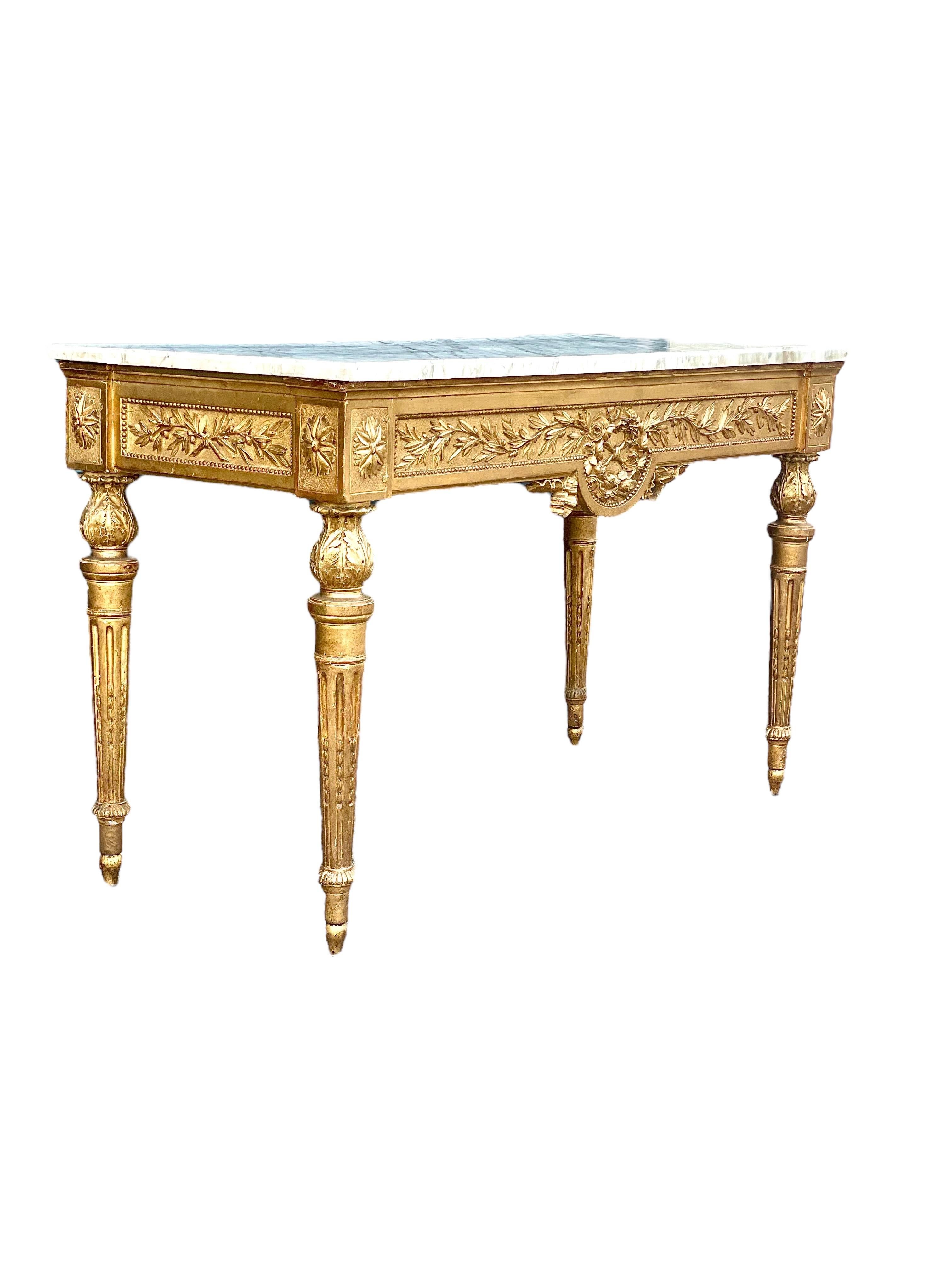 Opulente console en bois doré sculpté d'époque Louis XVI, avec son plateau en marbre d'origine, datant du XVIIIe siècle. De forme rectangulaire, cette élégante table néoclassique est minutieusement sculptée et décorée, sa ceinture étant ornée sur