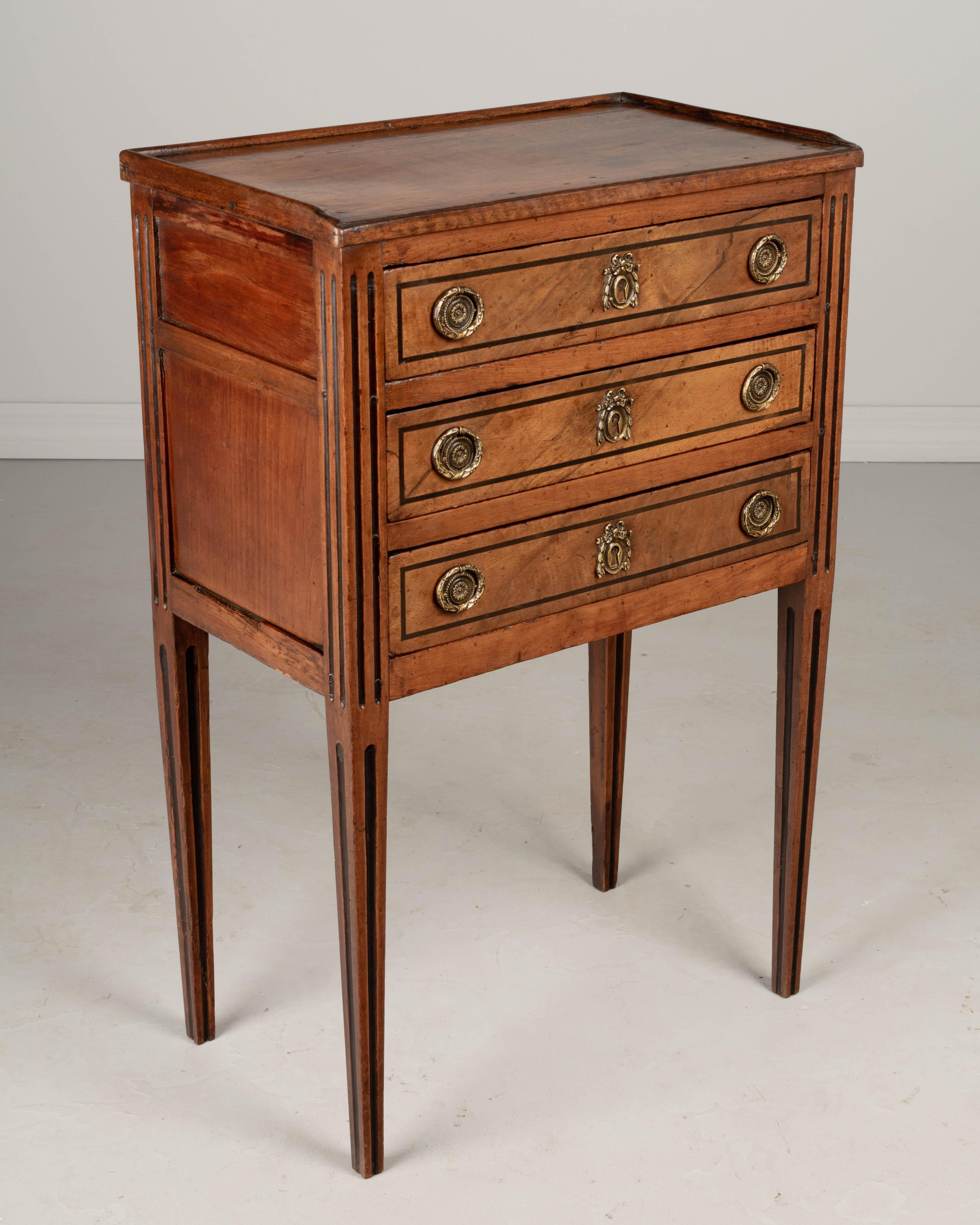 A late 18th century French Louis XVI Period side table made of solid walnut and cherry with black accent details. Three dovetailed drawers with original cast brass ring pulls. fine craftsmanship with traditional pegged construction. Elegant