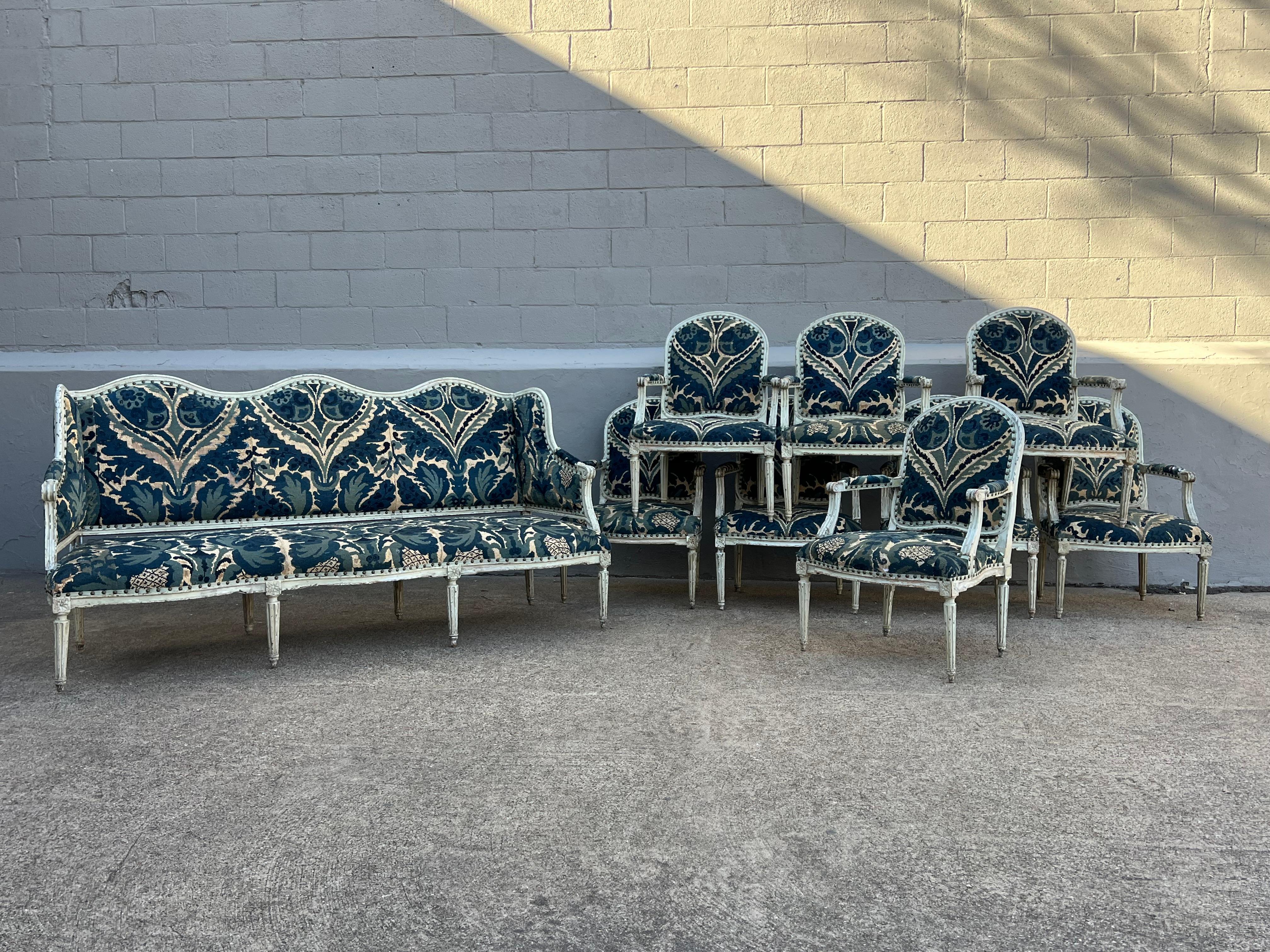 French nine piece Louis XVI period salon suite consisting of 8 armchairs - fauteuils and a sofa - canape with wings. This set is from the late 18th century and has an old painted finish with old paint showing through in layers. It is upholstered in