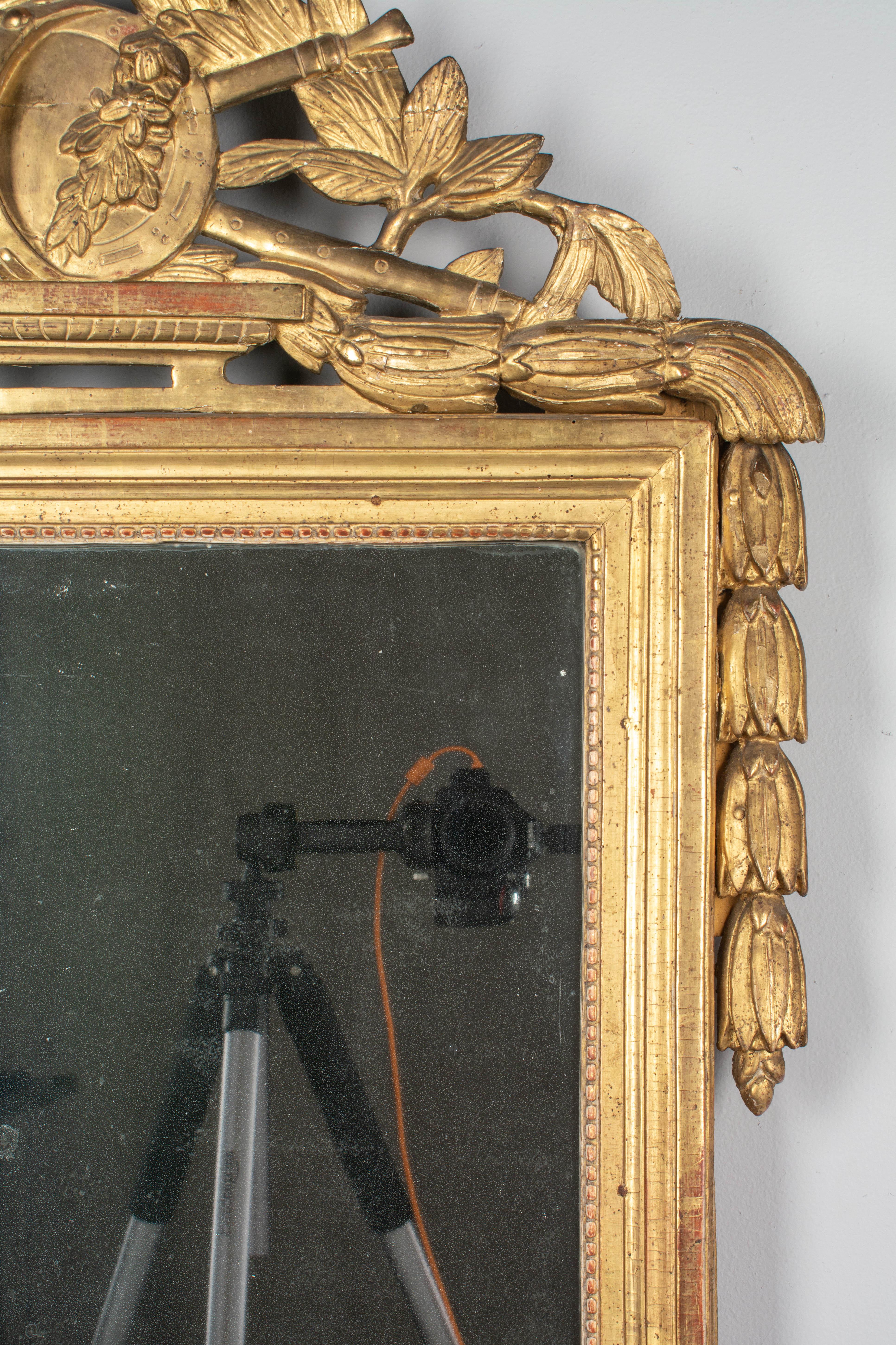 An 18th century French Louis XVI style giltwood mirror. Hand carved crest with musical instruments including a Horn, flute and tambourine, surrounded by leaves and floral garlands. In good condition with bright gilt finish. Mirror is original with