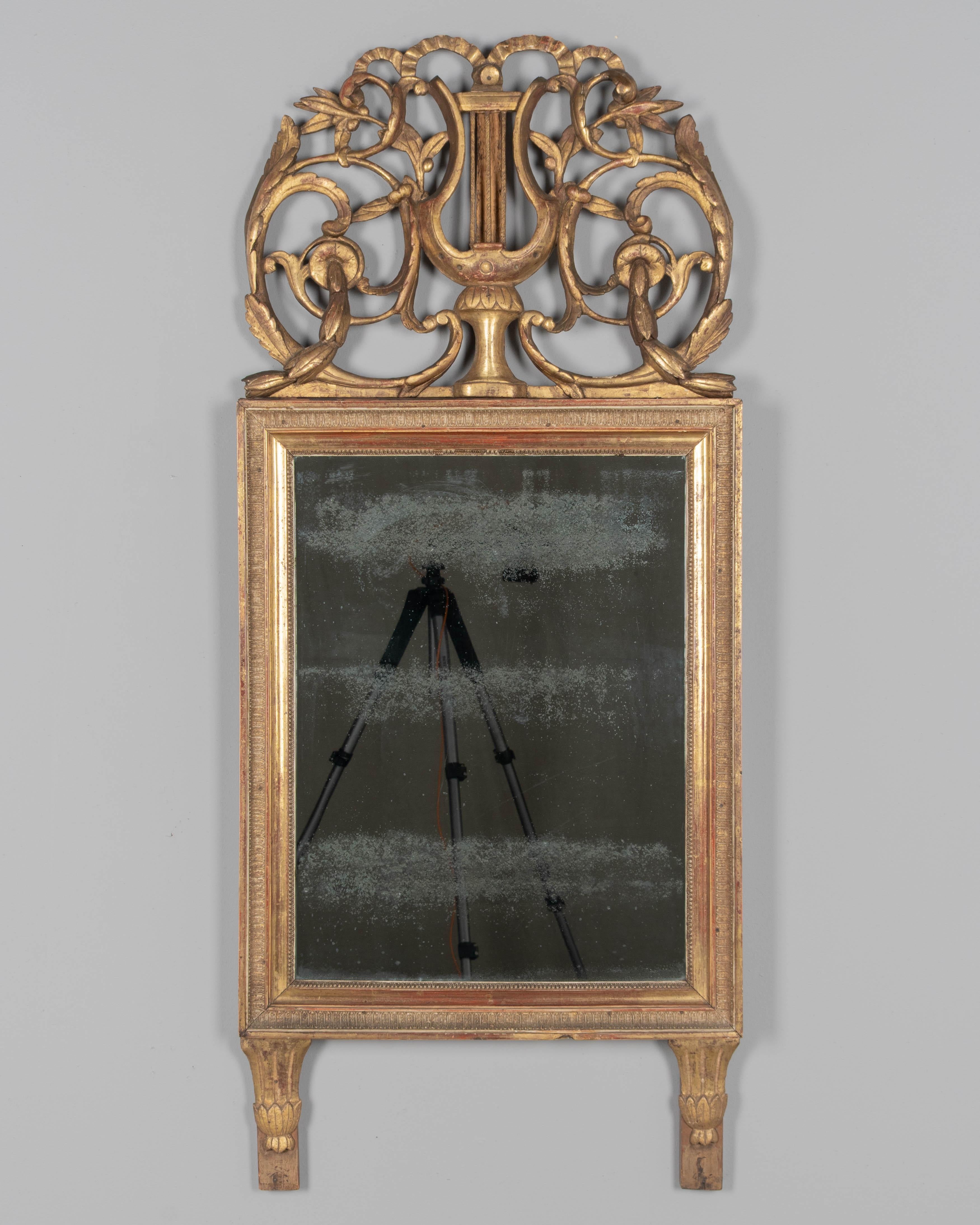 Espejo francés de madera dorada de finales del siglo XVIII, época Luis XVI. Cresta alta tallada a mano con lira, cintas y hojas de laurel en volutas. Todo original con restauración antigua en la cresta y pequeñas pérdidas. Cálida pátina dorada. Un