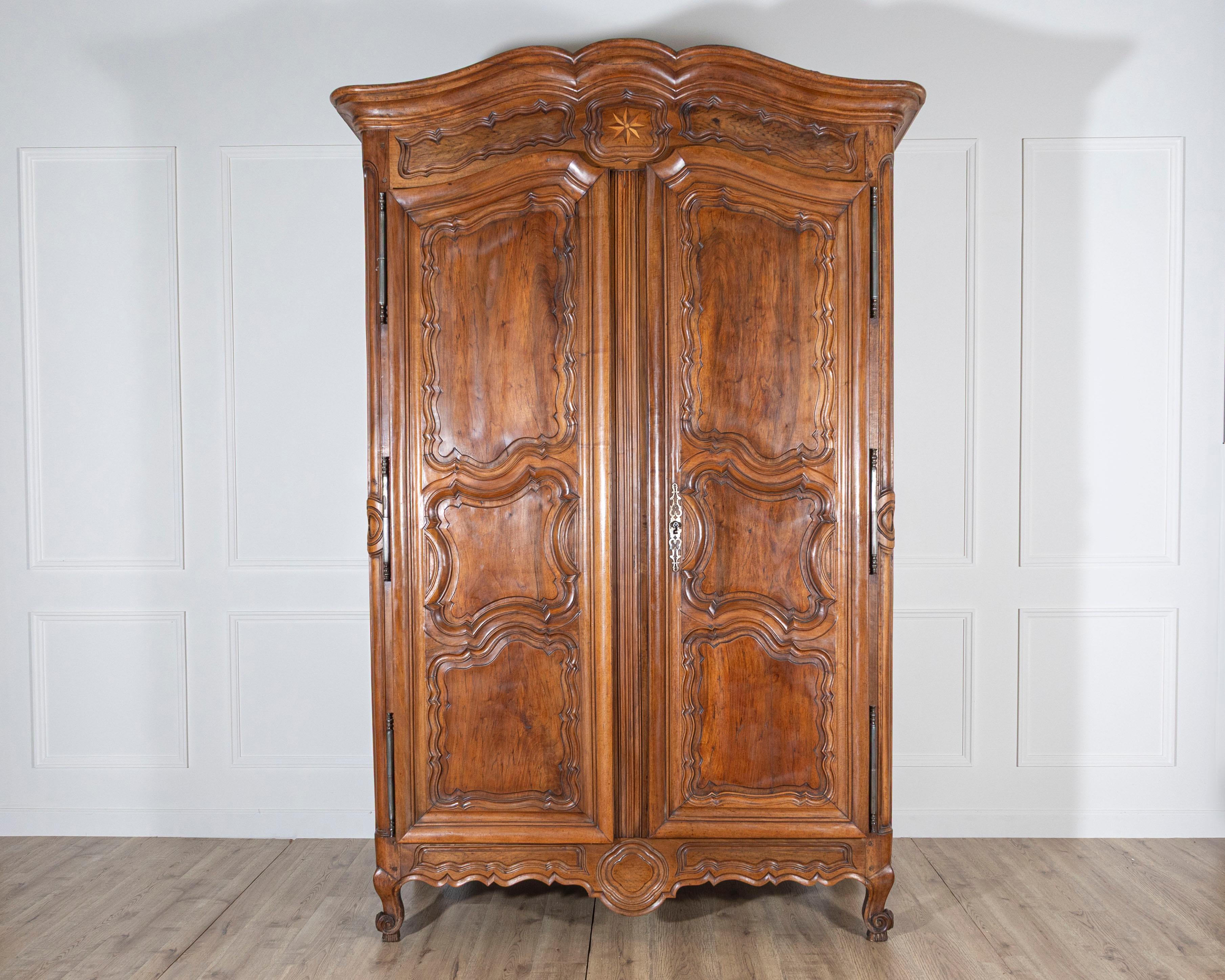 A magnificent and imposing Lyonnaise wardrobe from the 18th century, crafted in richly grained walnut and showcasing the opulence of provincial French cabinetry. This tall armoire features a striking double-arched cornice that sits gracefully above