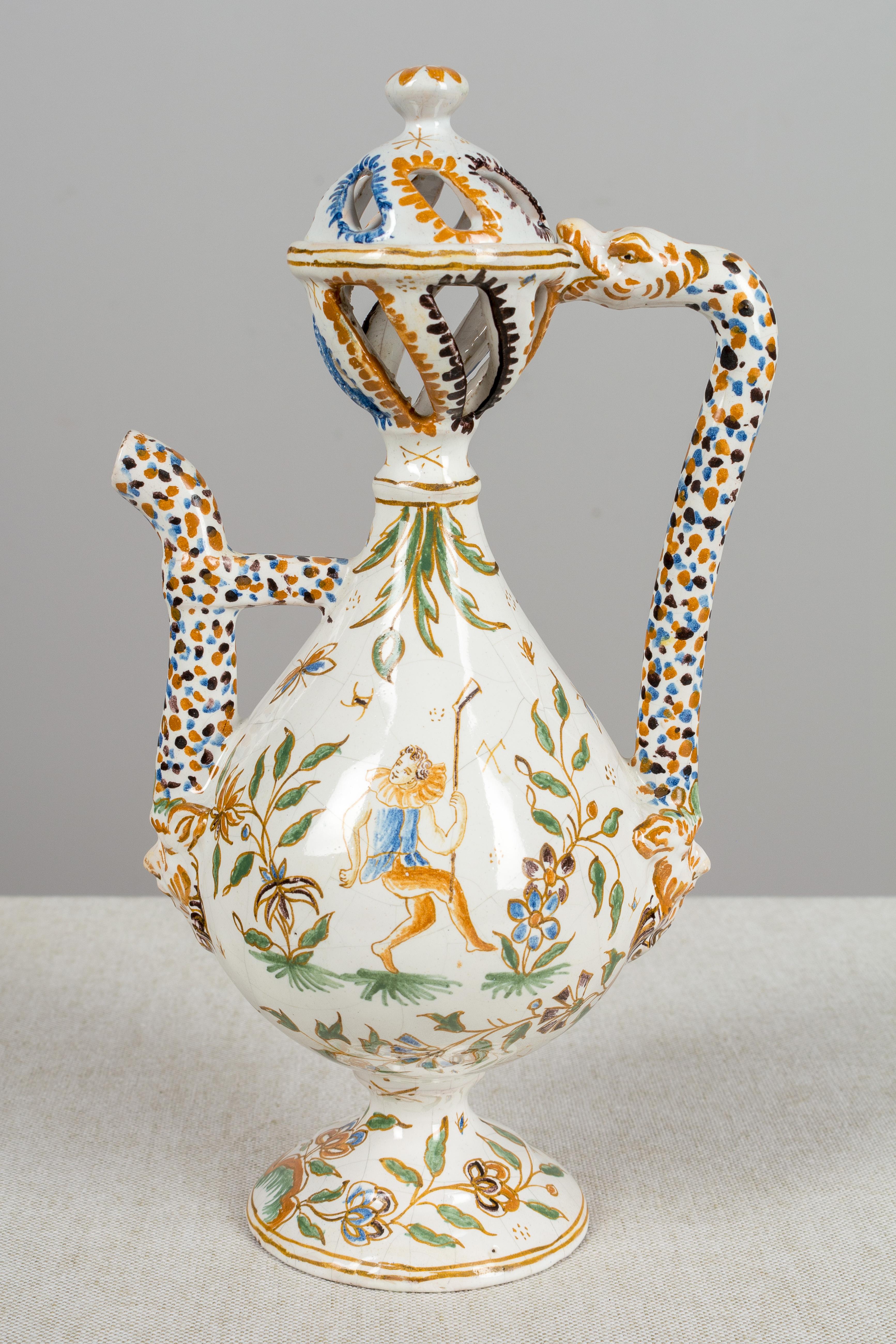 A small 18th century French Moustiers faience ewer with an unusual pierced dome lid. Delicate hand painted figural and floral decoration in the traditional colors of mustard yellow, green and blue. From the workshop of Joseph Olérys with mark on the