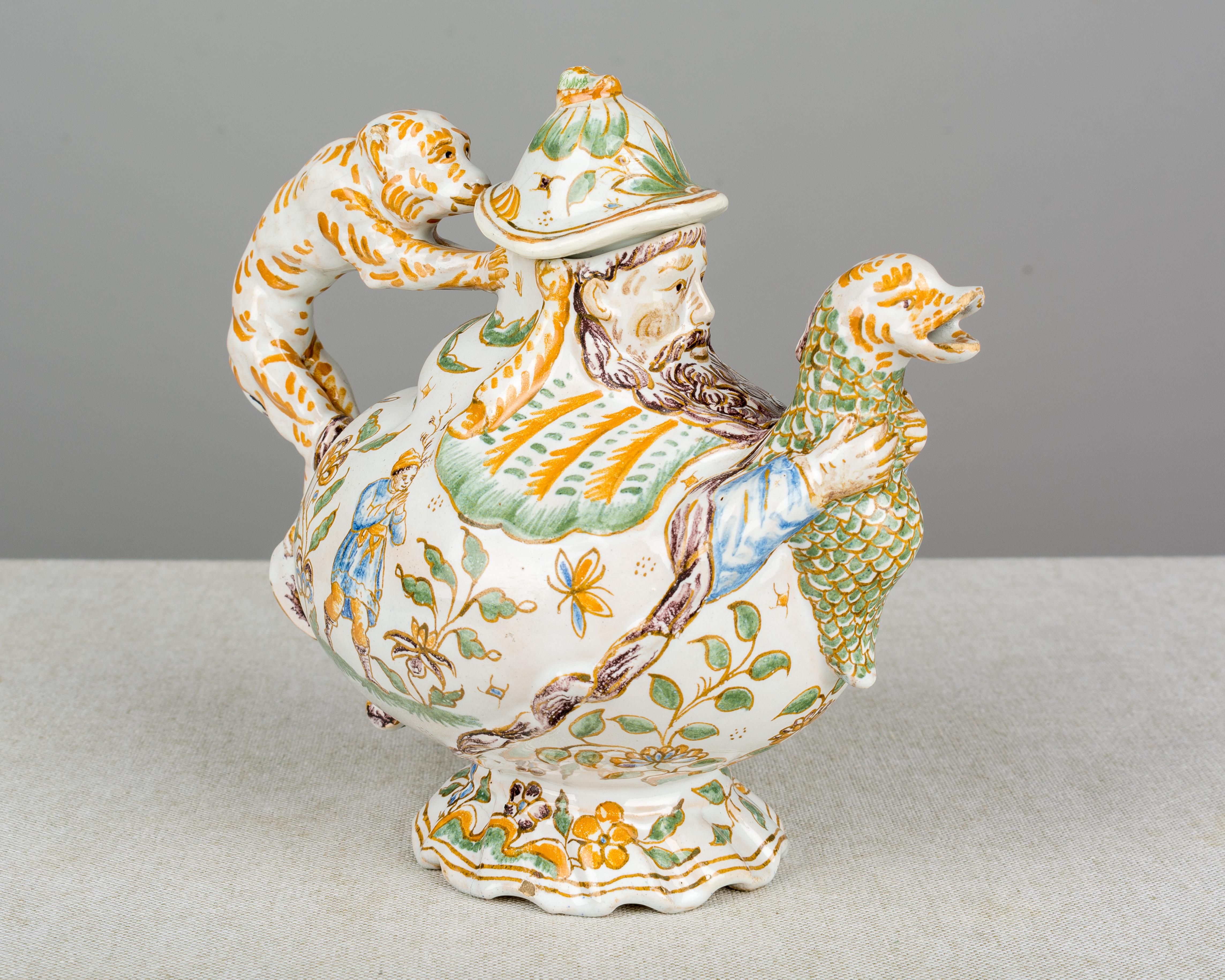 A whimsical 18th century French Moustiers faience teapot with monkey handle and dolphin spout. Delicate hand painted figural and floral decoration in the traditional colors of mustard yellow, green and blue. From the workshop of Olérys-Laugier with