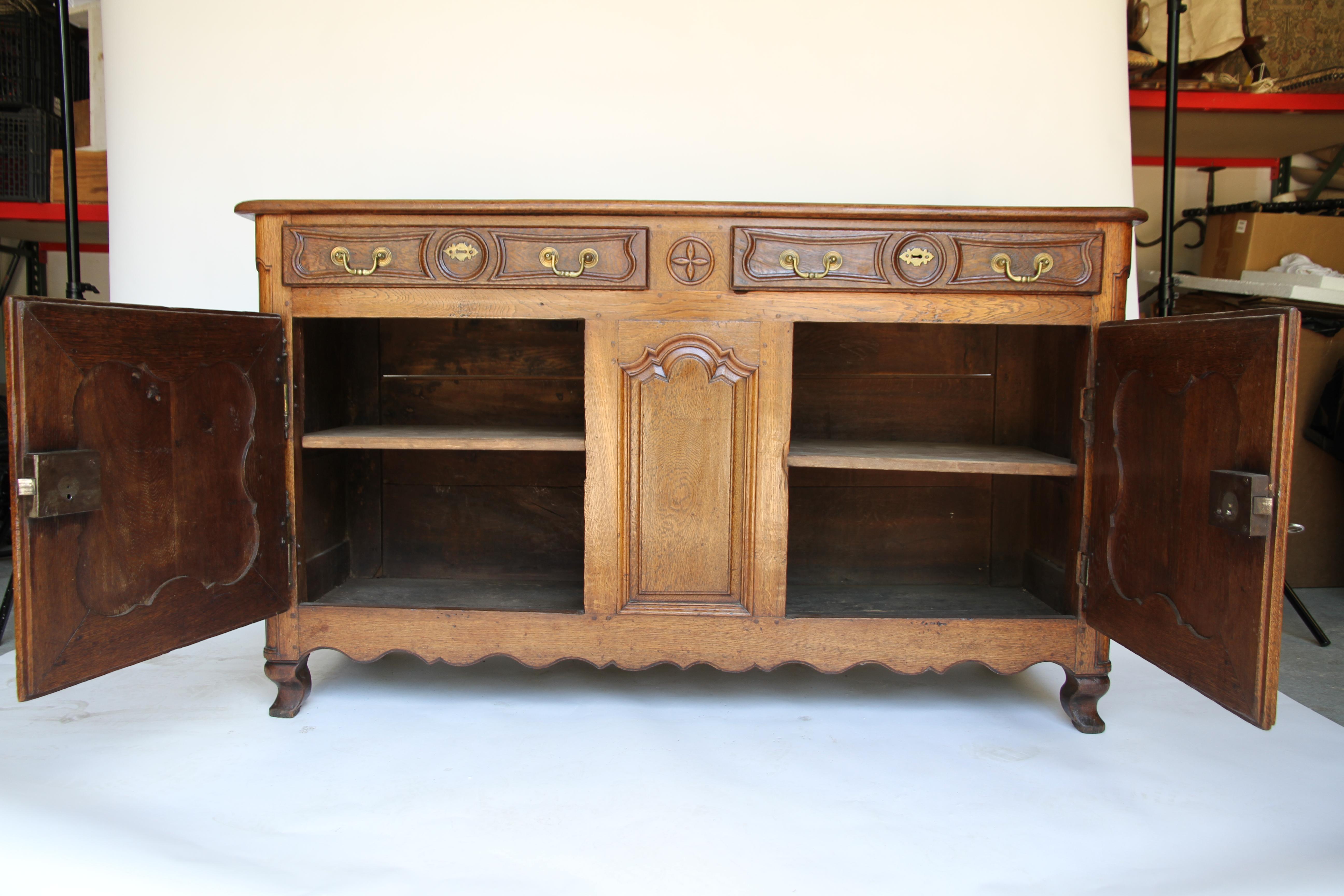 A beautiful antique French buffet featuring two drawers and two doors with brass drawer hardware and one key which unlocks both doors. The interior has one shelf. This piece is in wonderful condition and has a rich, beautiful patina.