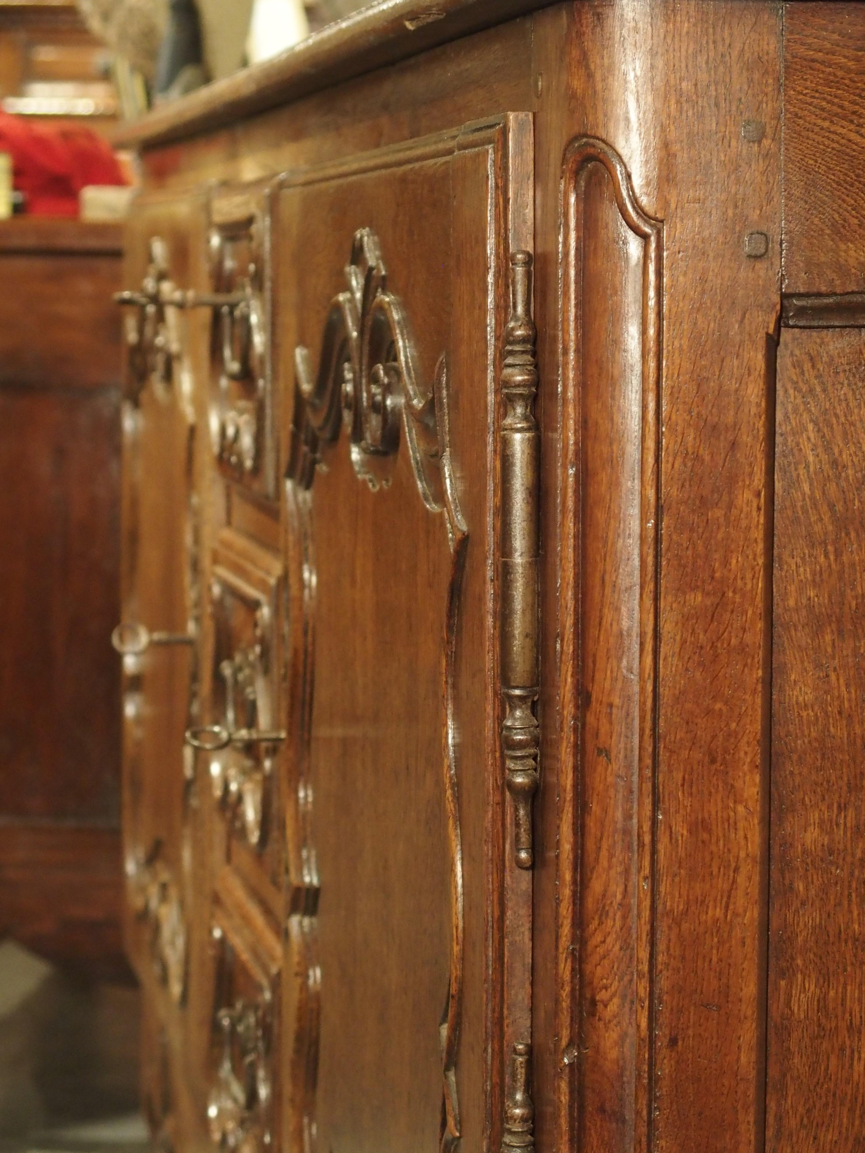 Sculpté à la main en France au cours des années 1700, cet étonnant buffet en chêne comporte deux portes sur charnières en fer séparées par trois tiroirs empilés verticalement. Cette orientation se retrouve souvent dans les buffets produits dans la