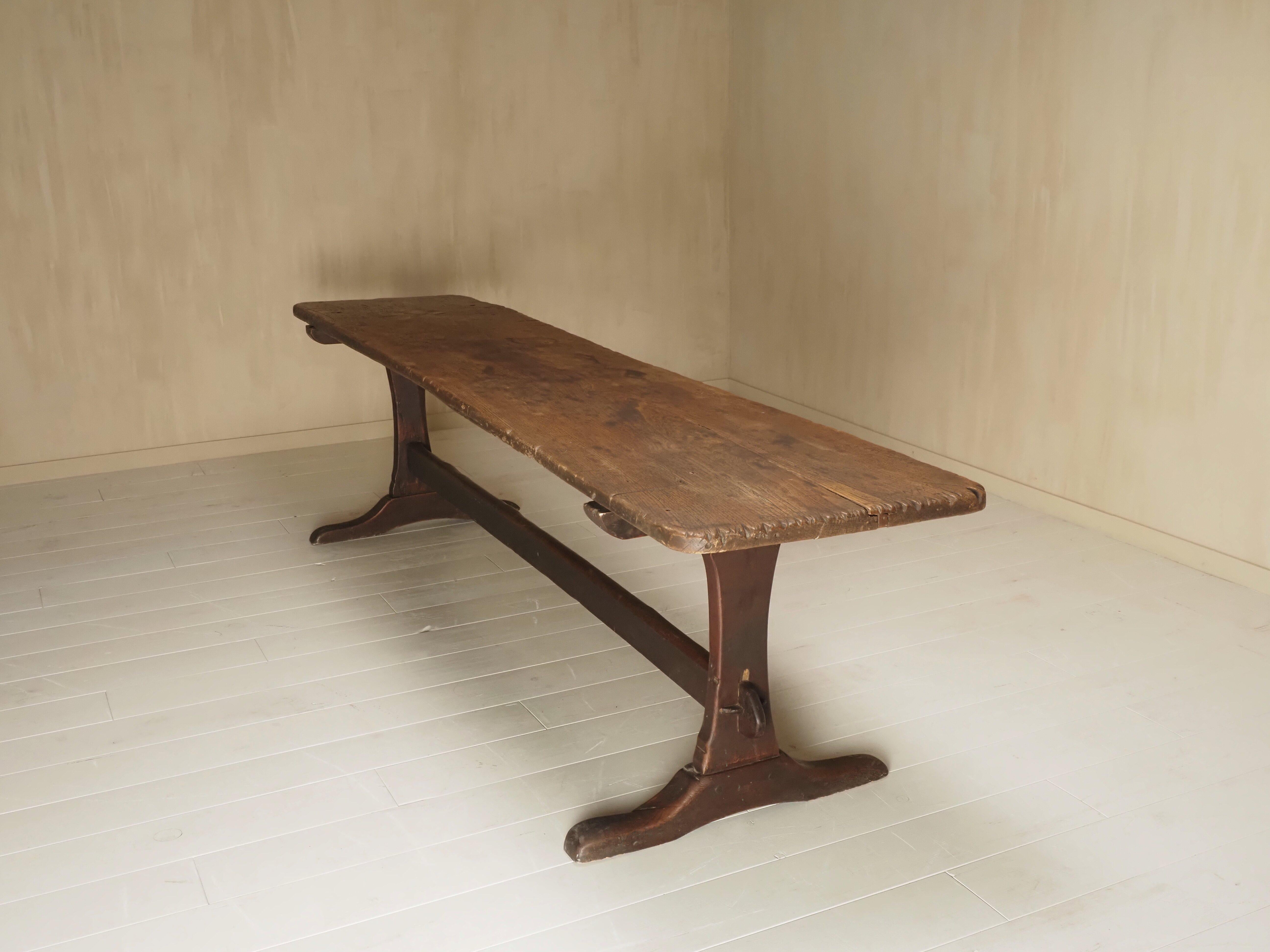 This is a beautifully worn 18th century French refectory table, handcrafted from solid oak. The table features a long, narrow top made from one slab of wood, resting on two sledge-style trestle legs connected by a central stretcher. The surface