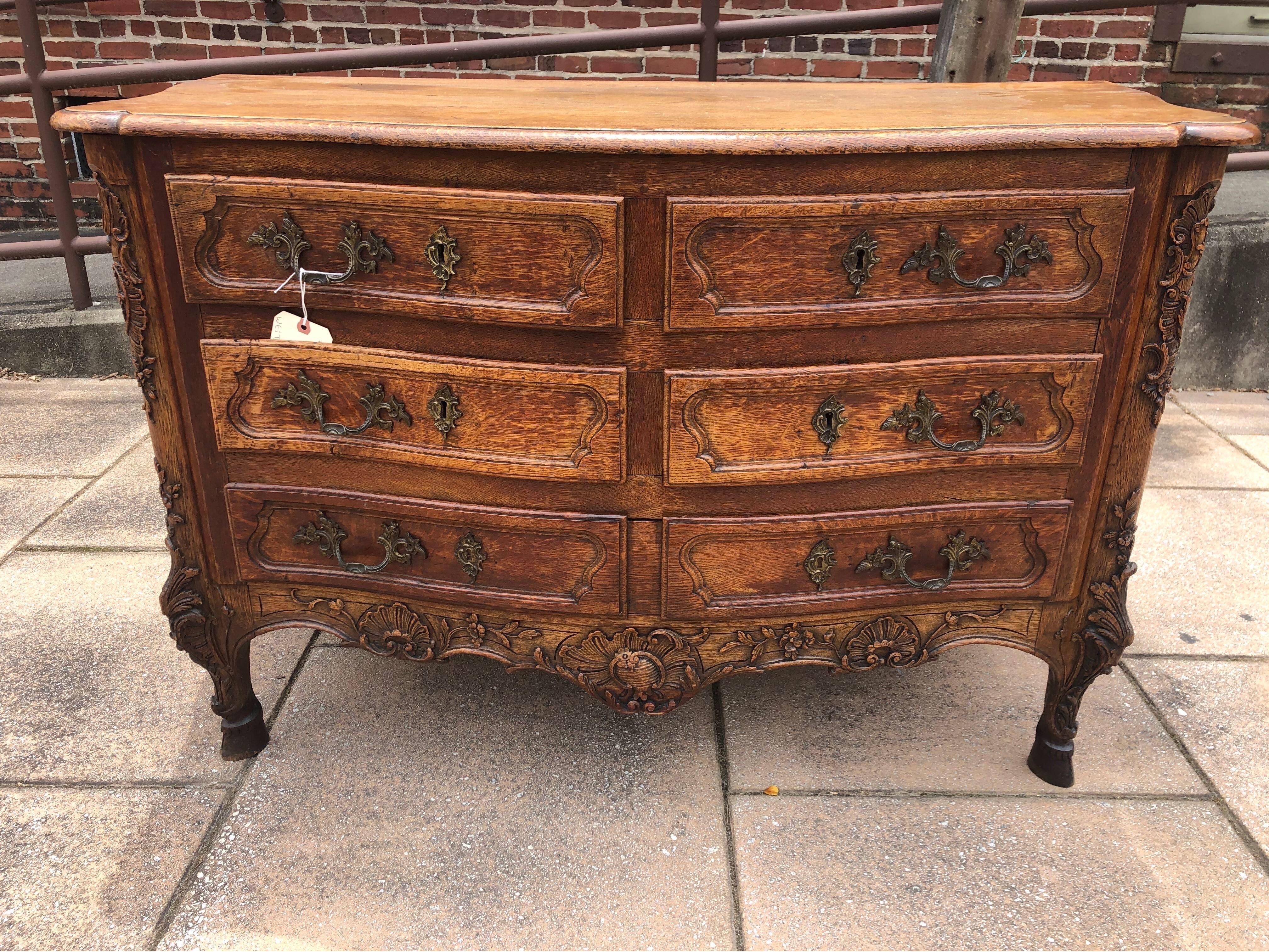 18th century French carved oak serpentine commode on hoof feet. 4 smaller drawers over one larger drawer with handsomely carved apron, knees and feet. Scrolls, foliage and shells carved throughout and resting on well defined hoof feet.