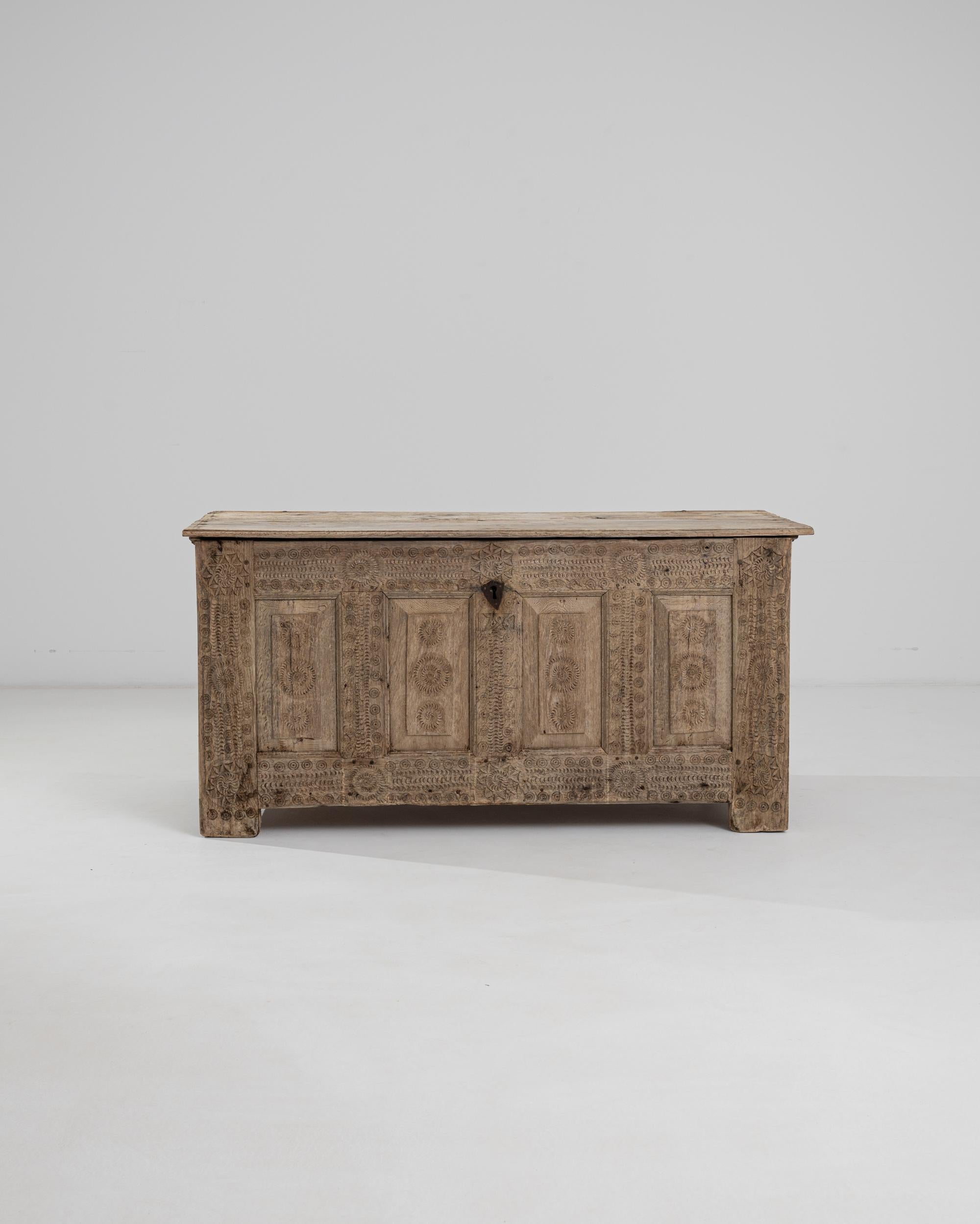 An antique trunk in natural oak, decorated with delicate carvings lend this piece a gothic demeanor. Built in France in the 1700s, the front panel is covered with rippling, geometric motifs of circles, sunbursts and crescent moons. They appear to