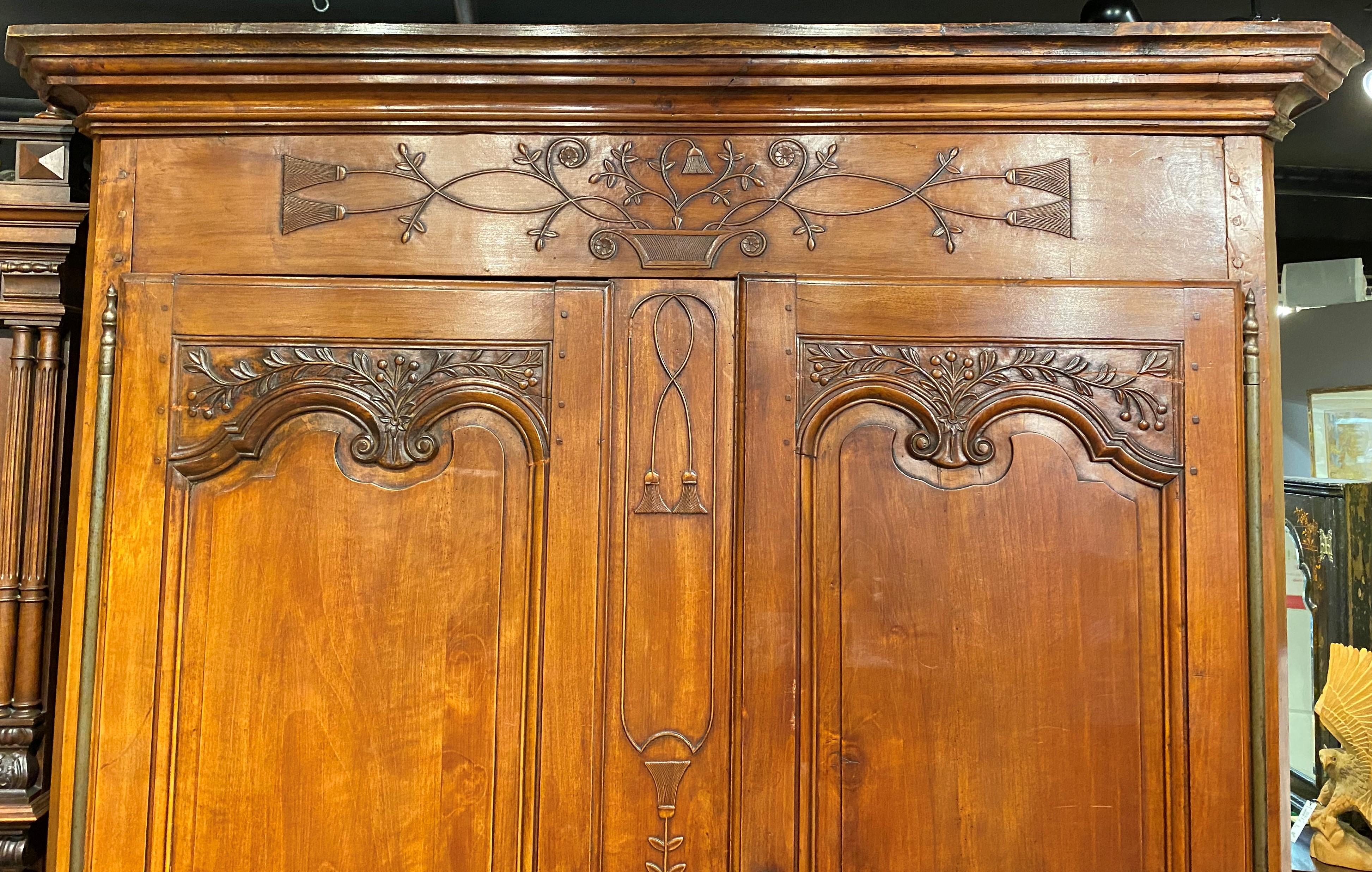 A beautiful two-door French armoire with detailed tassel and foliate carved basket frieze decoration, continued around scrolled brass door escutcheons and door panels, over a nicely carved skirt, all supported by short cabriole scroll carved legs.
