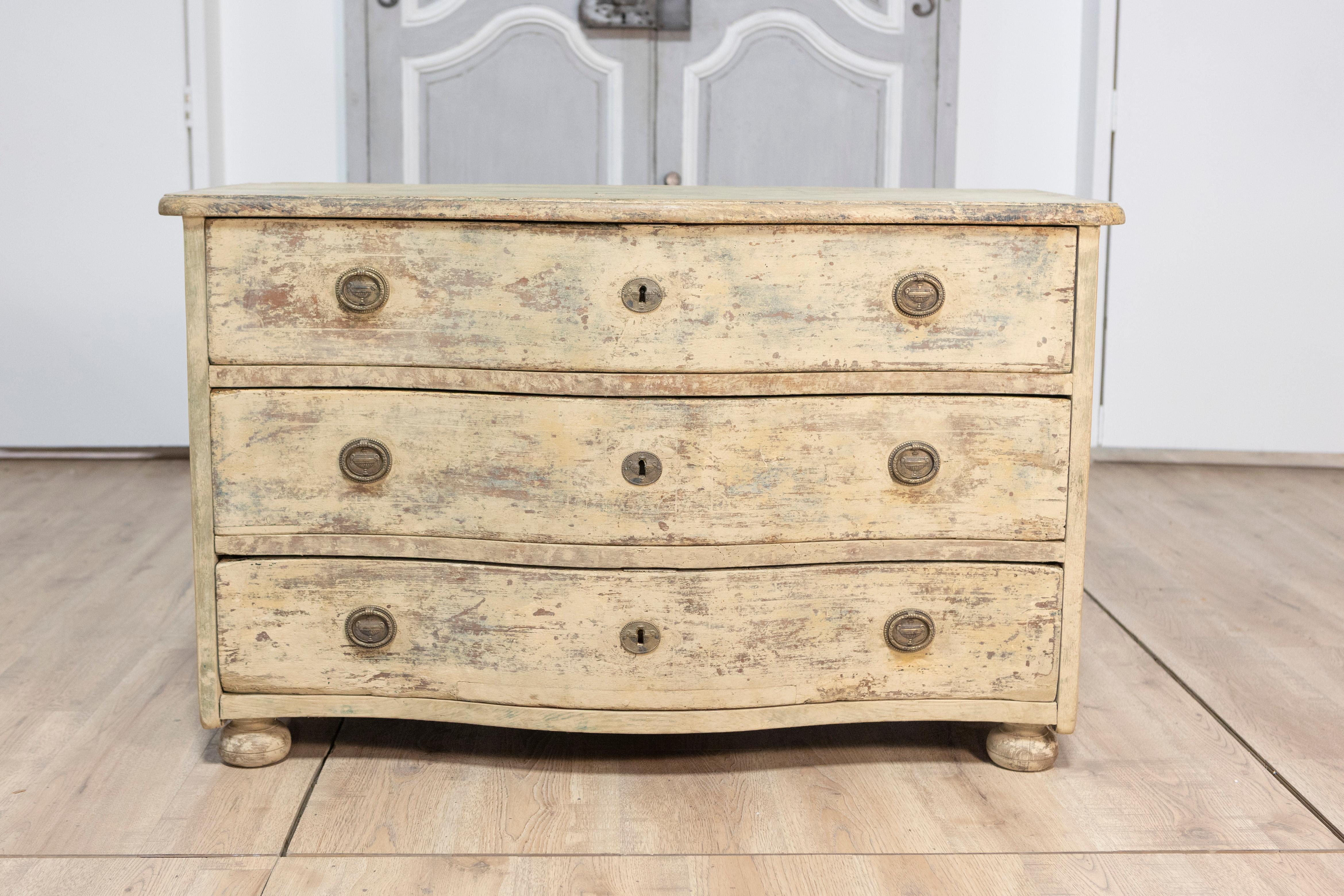Questa commode dipinta francese del XVIII secolo, risalente al 1760 circa, è uno splendido esempio di artigianato antico e di eleganza senza tempo. Realizzato in legno di pino, il mobile presenta un fronte a serpentina con tre cassetti, ognuno dei