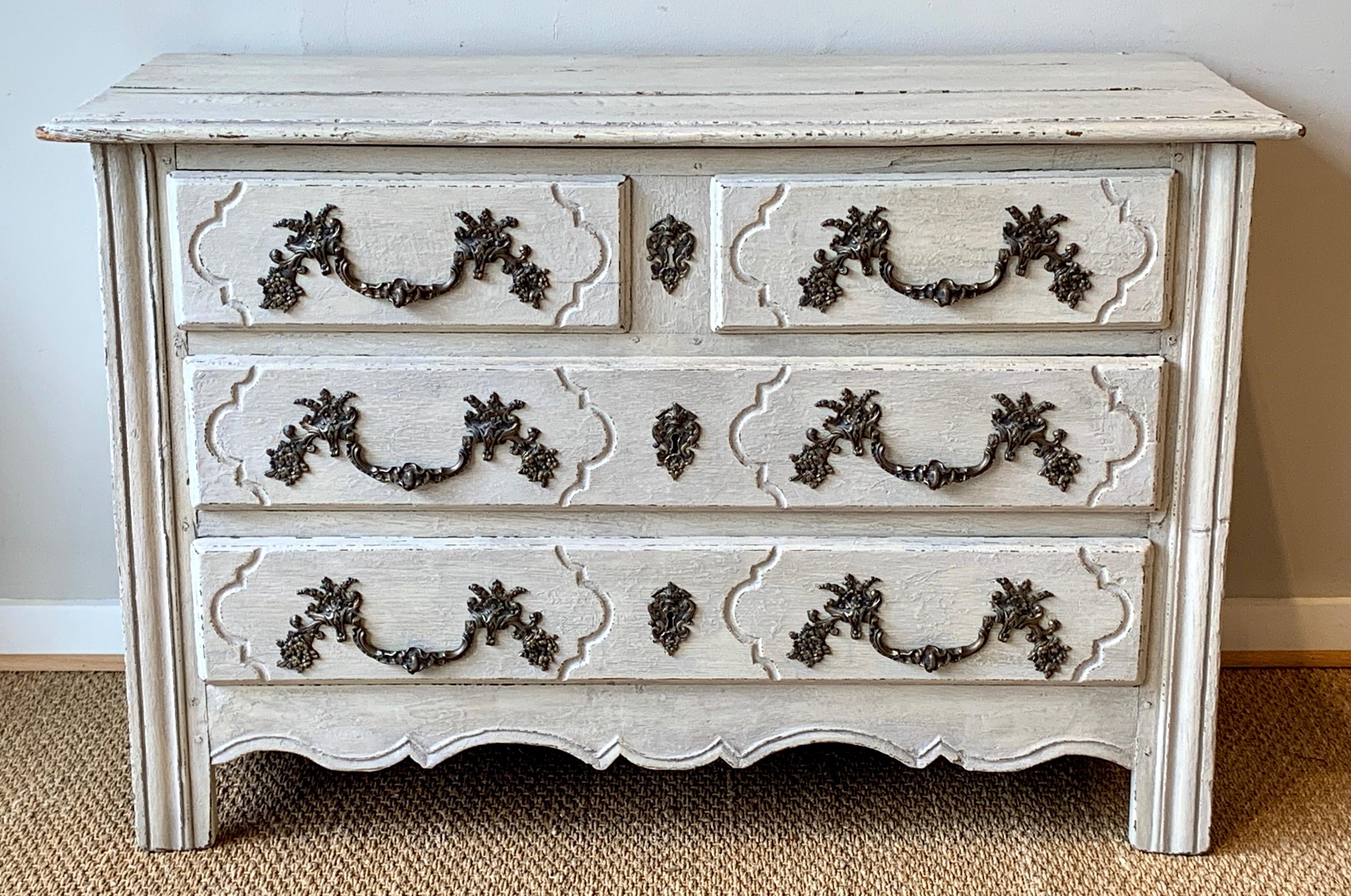 A late 18th century French carved and painted four-drawer oak commode in a soft gray paint with later cast brass pulls.