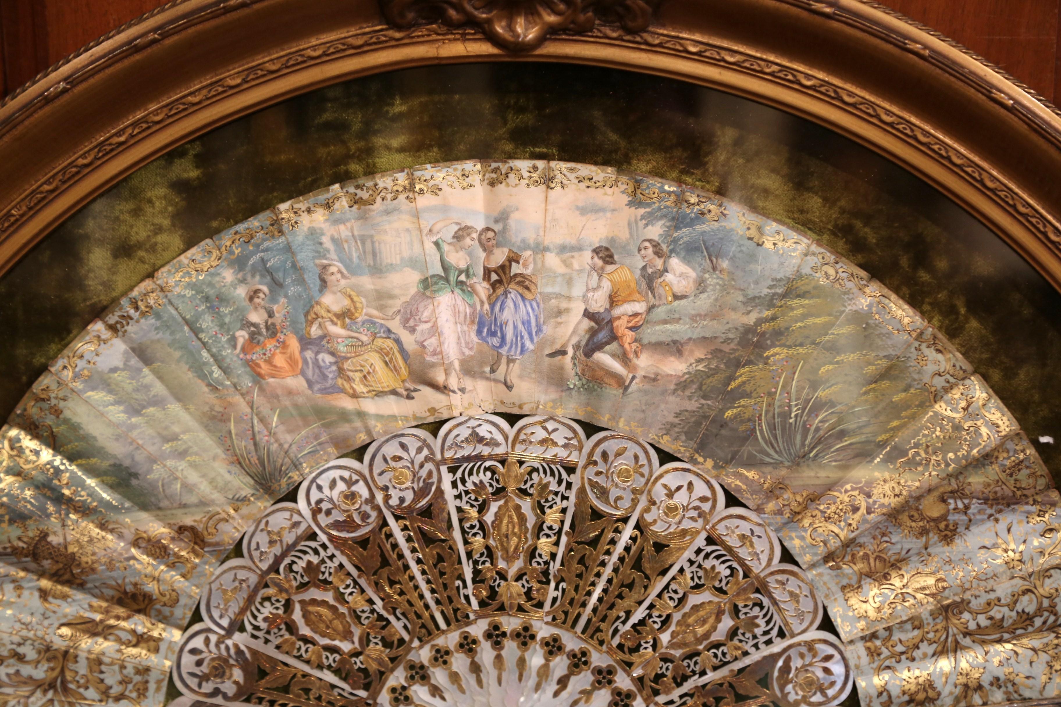 This ornate, antique paper and mother of pearl hand fan was crafted in France, circa 1780. The Rococo style fan is hand painted with bucolic courting scenes, and is embellished with luxurious gilt accents. The delicate hand fan is encased in glass