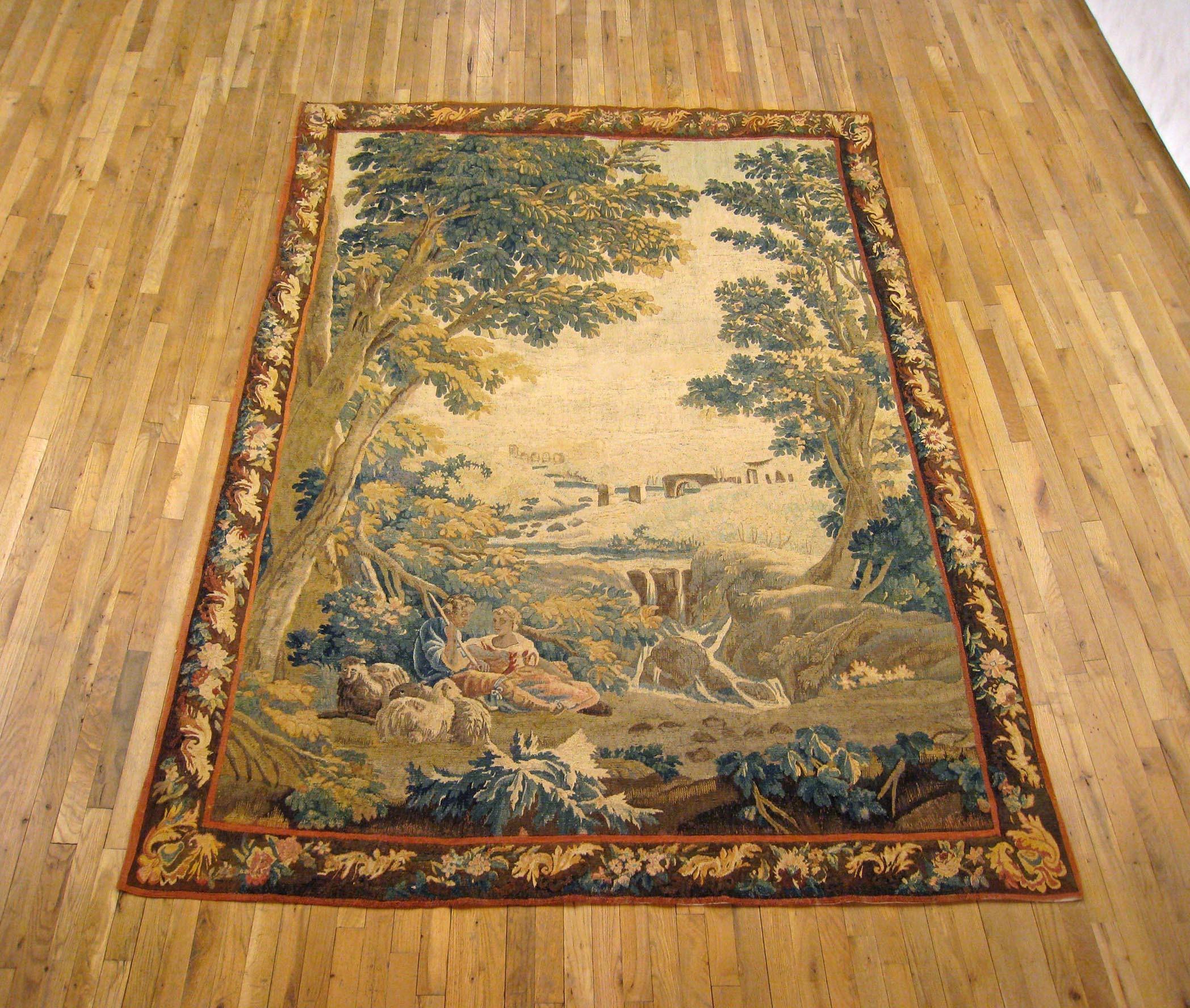 A French pastoral landscape tapestry from the 18th century, depicting a placid country scene with a young couple conversing and tending to their flock of sheep amidst the beauty and tranquility of the verdant landscape, and a murmuring brook flowing