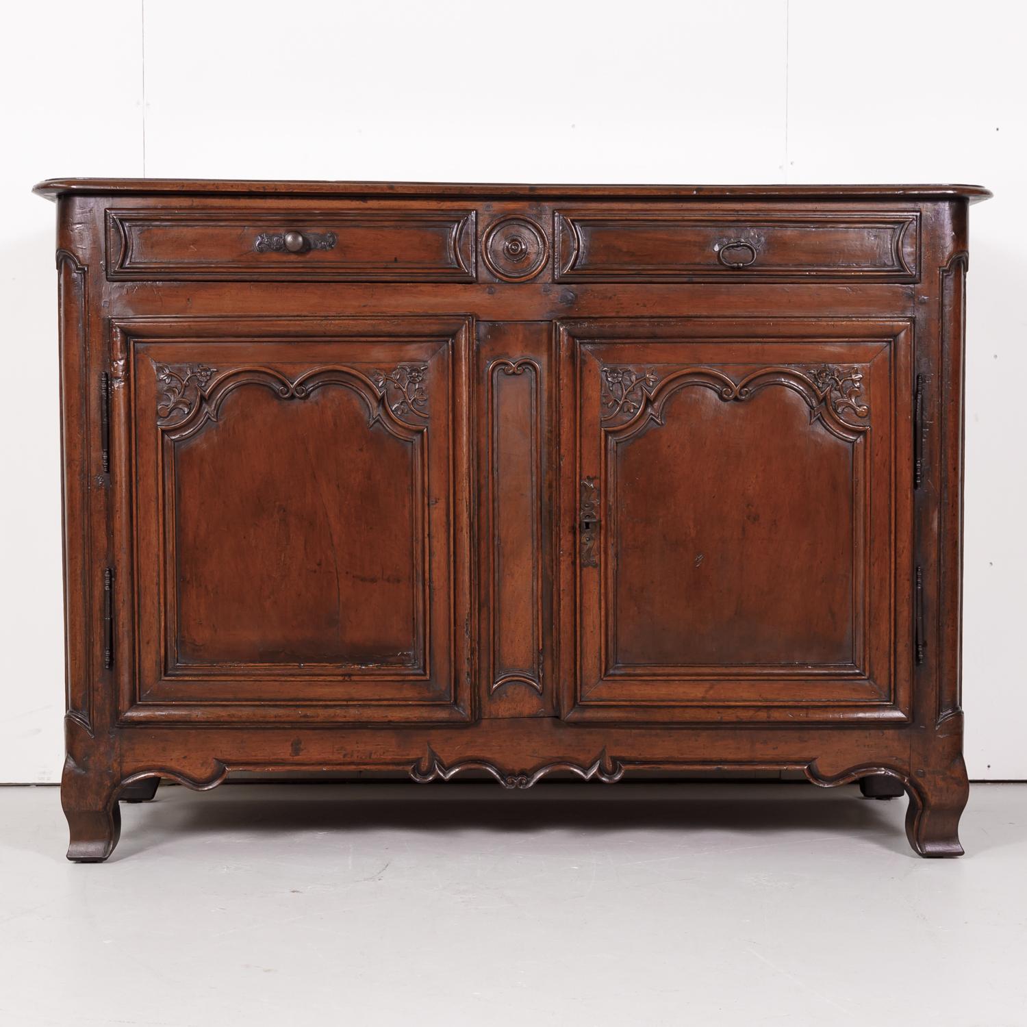 Lovely 18th century French period Louis XV solid walnut buffet handcrafted in Lyon, circa 1750s, having two doors over two drawers with floral and foliate carving on each recessed panel door. Carved apron raised on short cabriole legs. Single