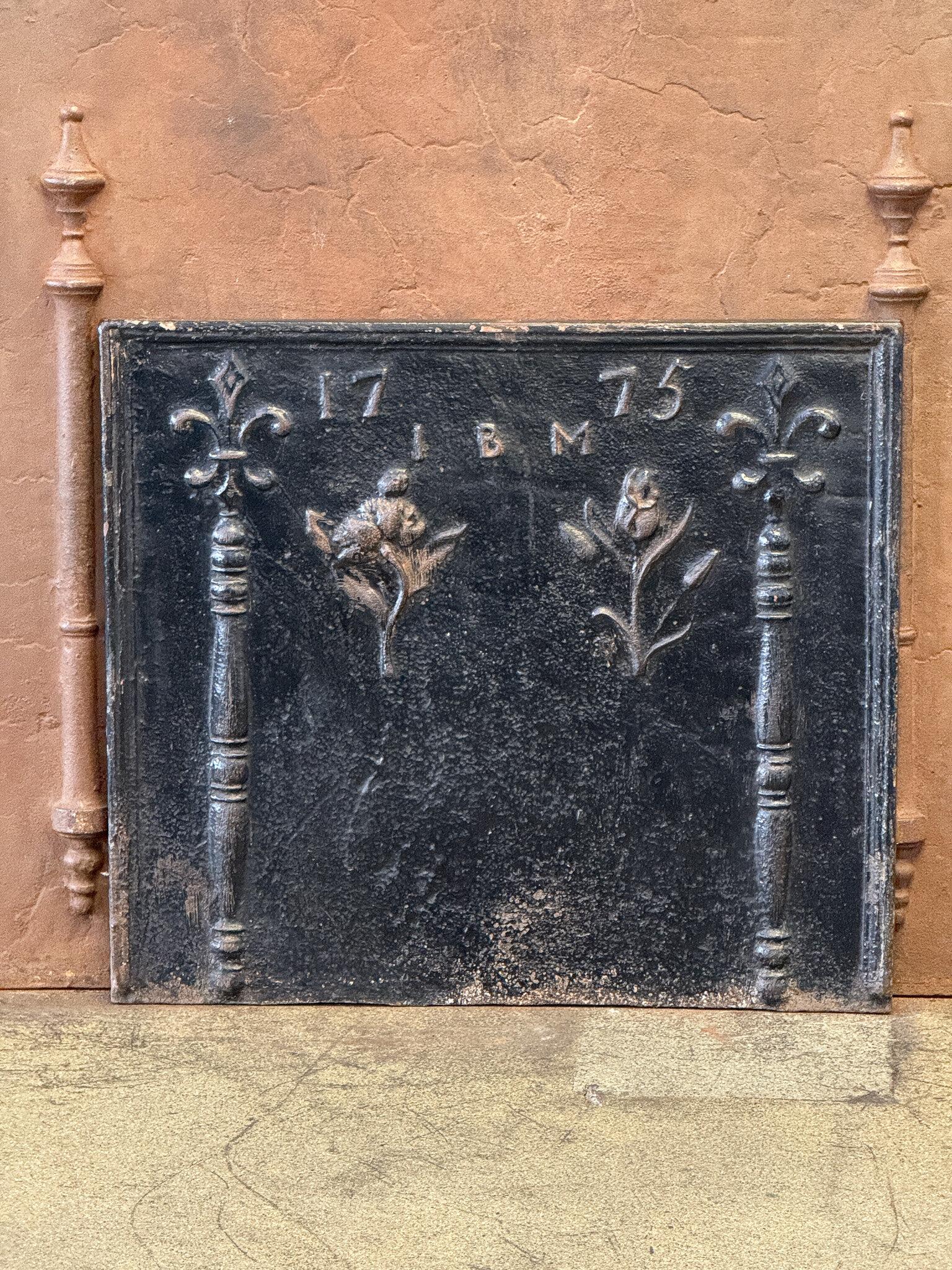 French fireback with two decorated pillars with fleurs de lys (lilies), two tulips, and the date of production 1775. Also the initials of the person who commissioned the production of the fireback can be seen. The fireback is of the Louis XV