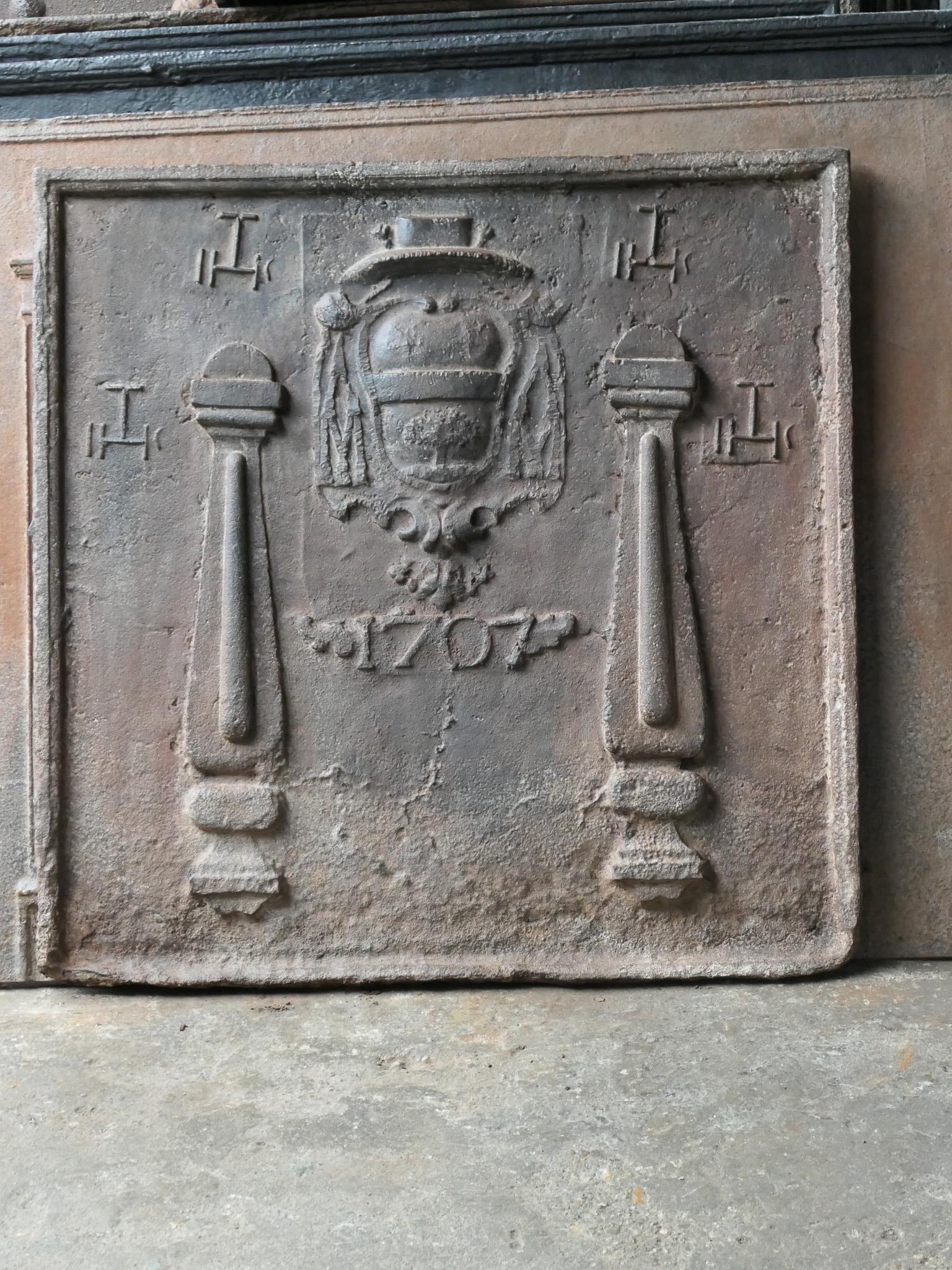 Plaque de cheminée française du XVIIIe siècle de style Louis XIV avec deux piliers, quatre monogrammes IHS et la date de production 1707. Au centre se trouvent les armoiries d'un évêque ou d'un cardinal. Le blason a été en partie tronqué lors de la