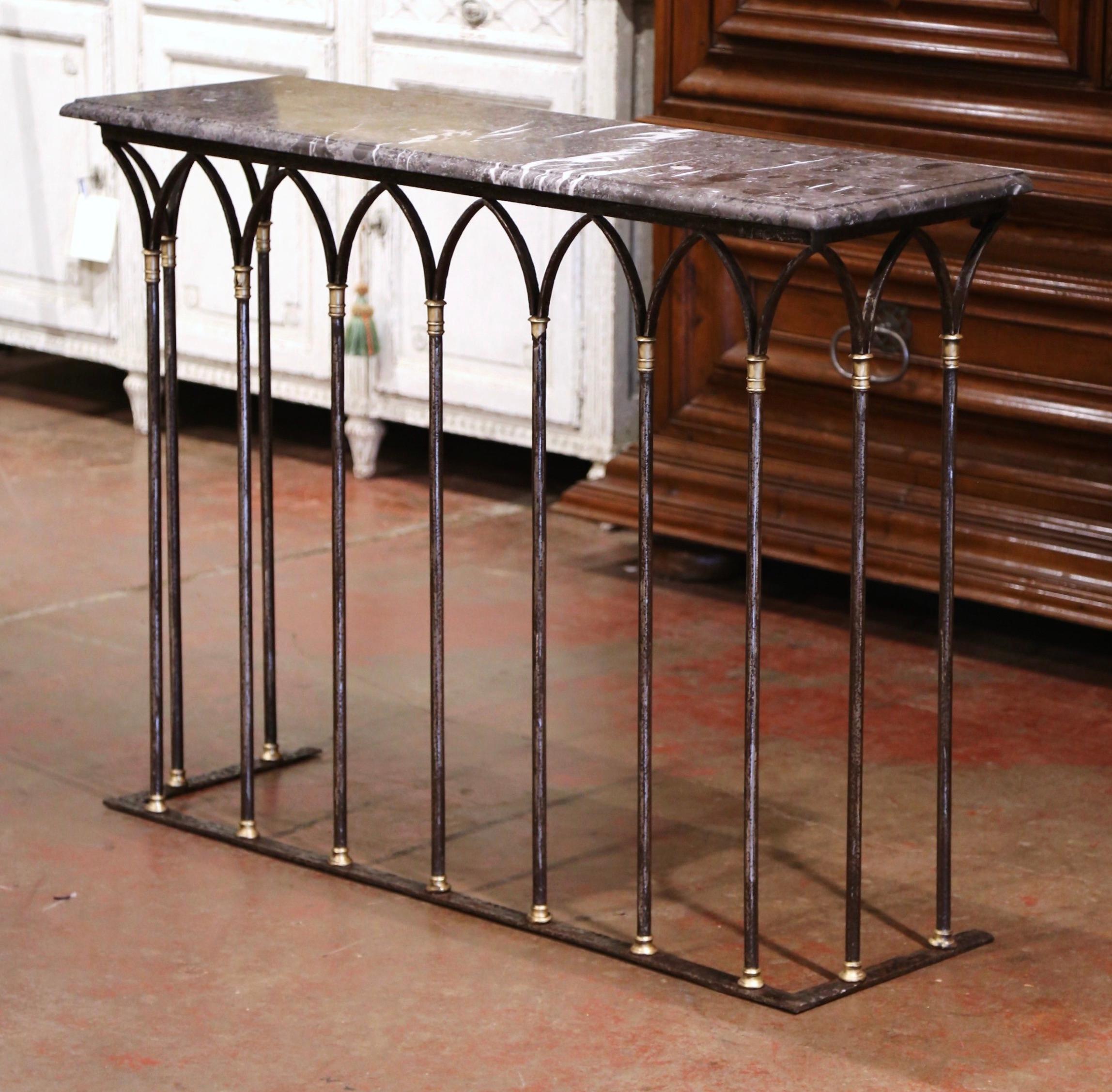 Crafted in France circa 1780, the antique console table features intricate forged cathedral shaped columns on all three sides embellished with decorative bronze rings at the top and bottom. The rectangular table is dressed with a thick variegated